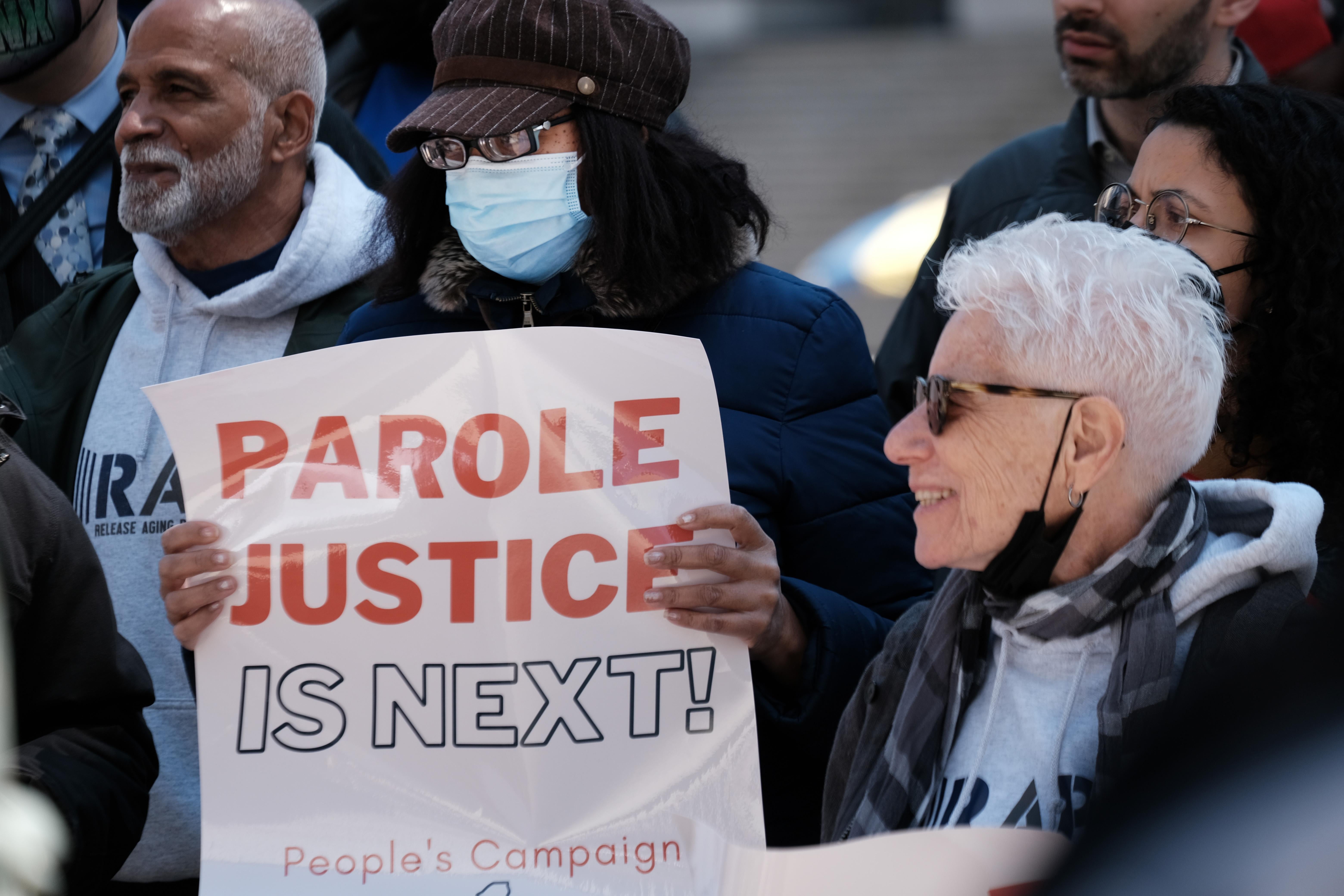 A woman holds a sign that says "PAROLE JUSTICE IS NEXT."