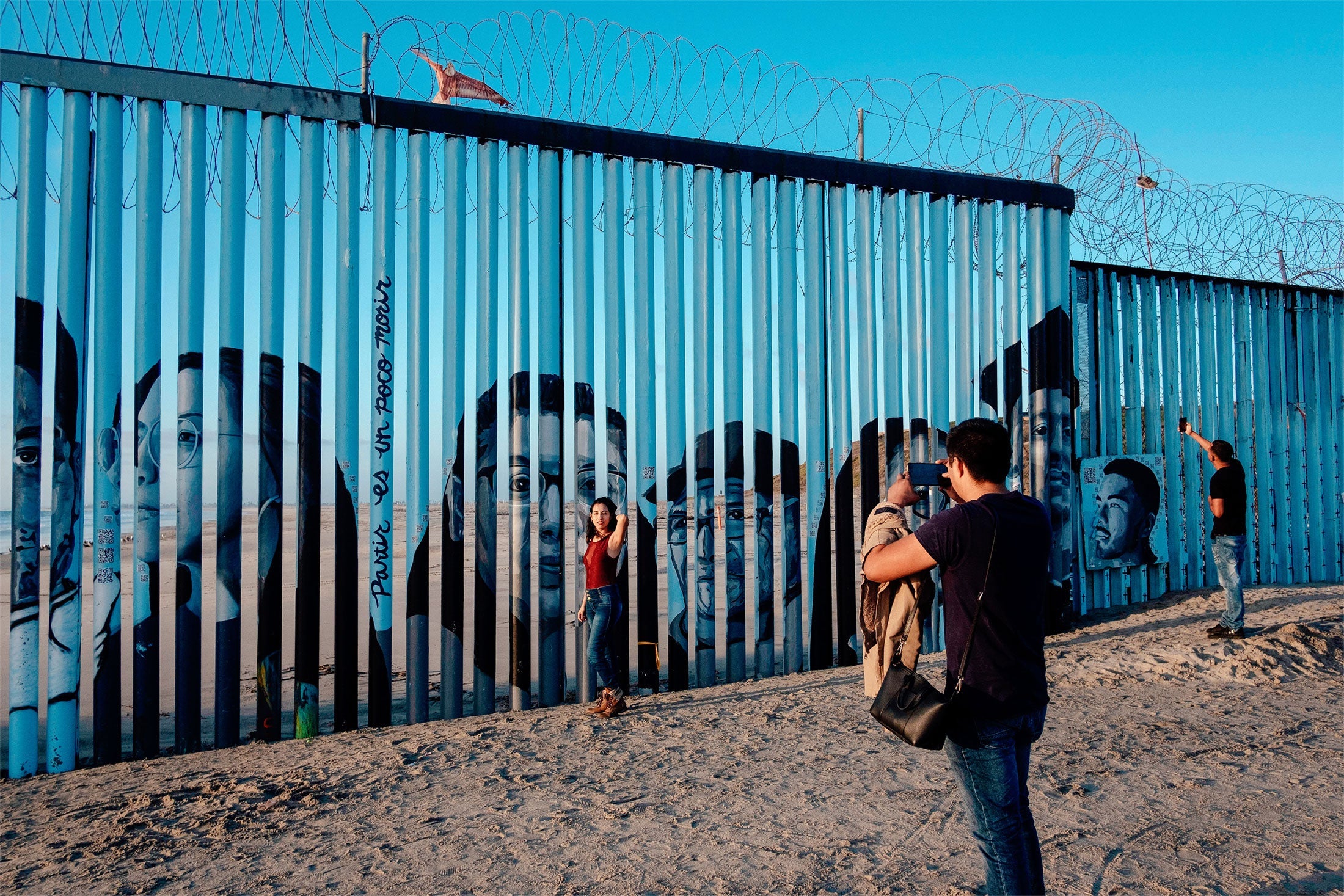 A visitor takes a picture of a woman posing in front of the US-Mexico border fence in Playas de Tijuana.
