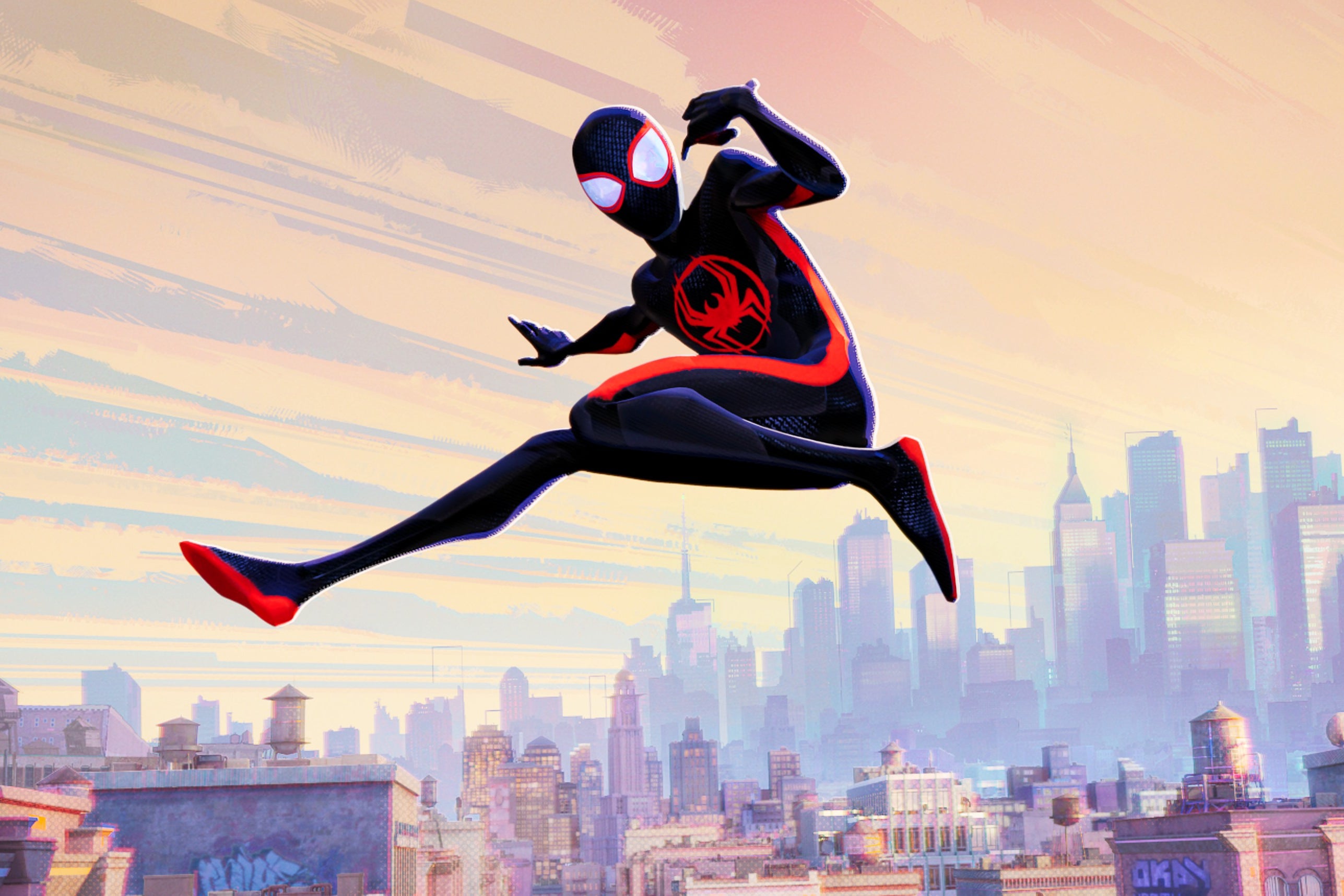 An animated from Spider-Man: Across the Spider-Verse shows Miles Morales, in his mostly black spider-suit with red racing stripes on the side, looking toward the camera while leaping against a sunset cityscape