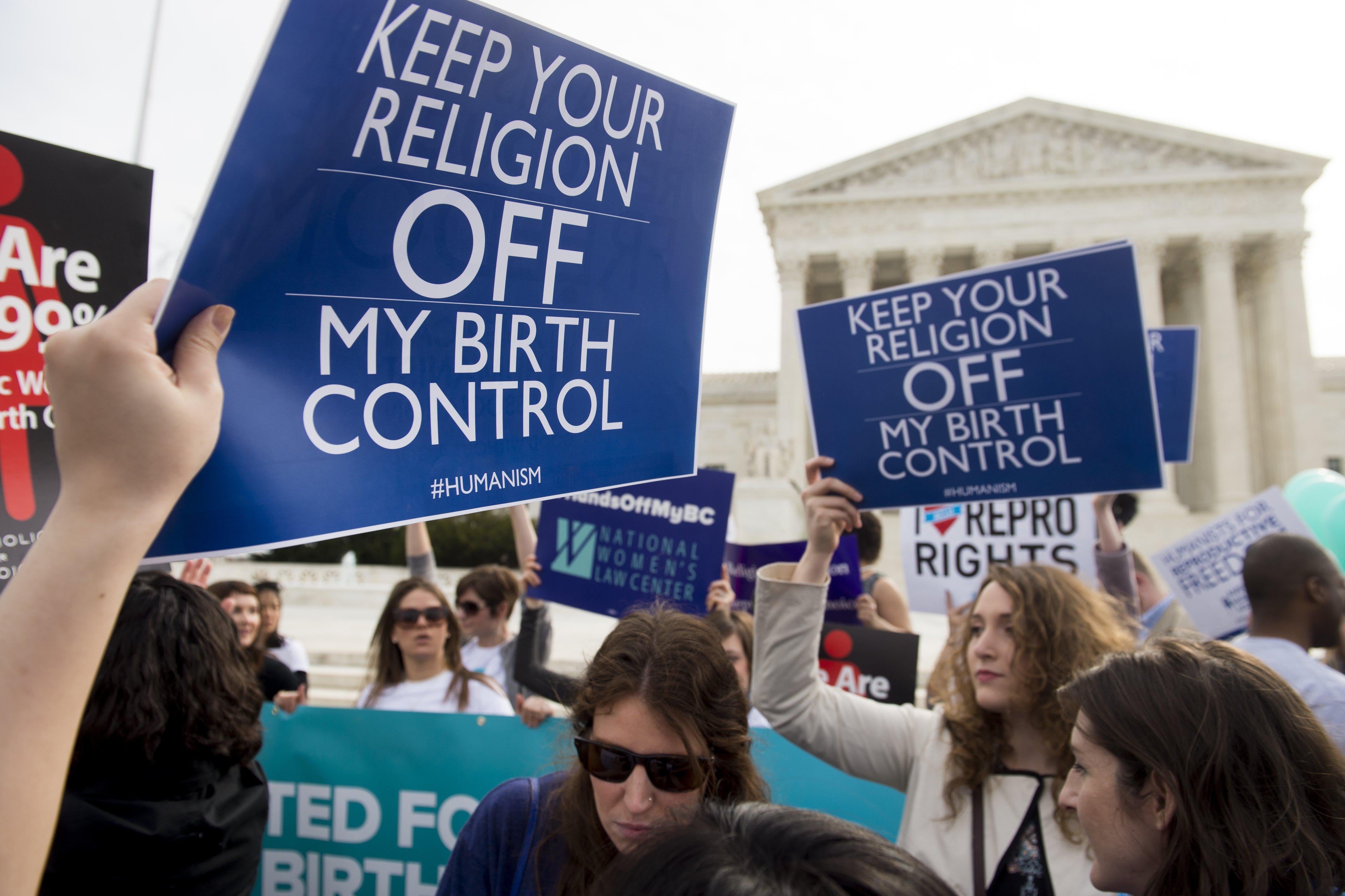 Protesters in front of the Supreme Court hold signs that read "Keep Your Religion OFF My Birth Control."