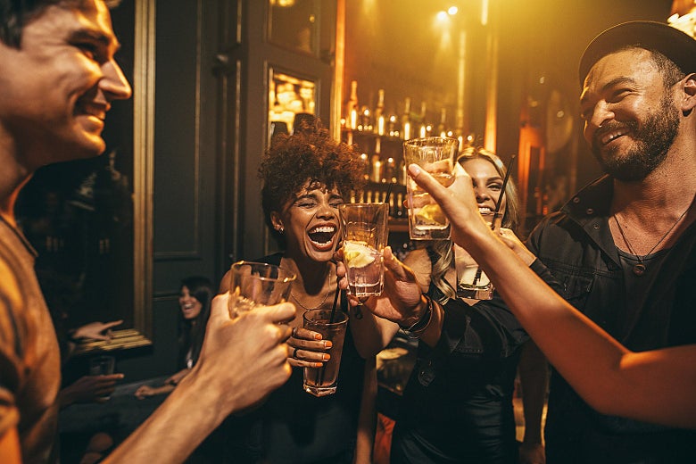 A group of maskless young people smiling and toasting at a bar.