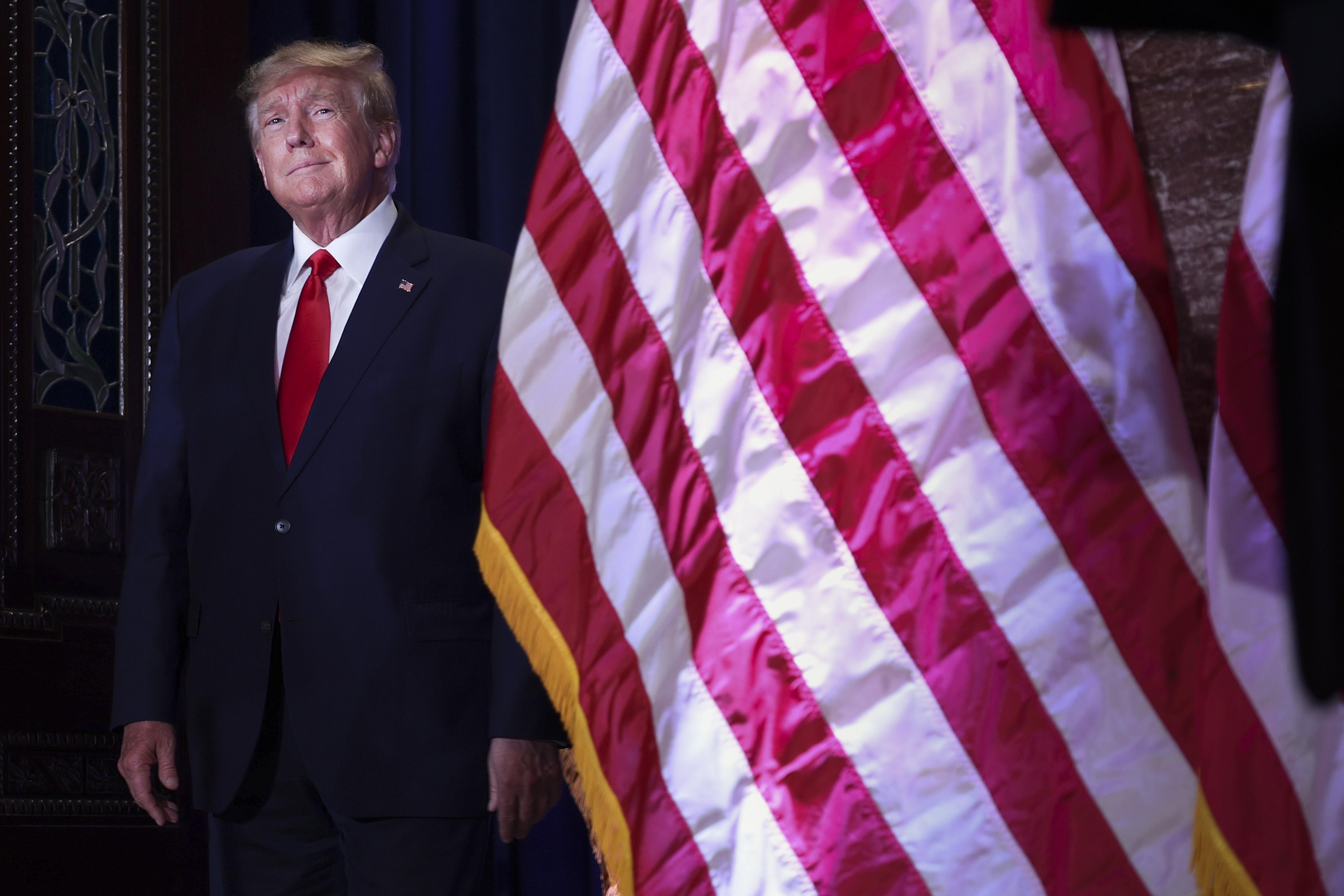Former U.S. President Donald Trump stands next to an American flag.