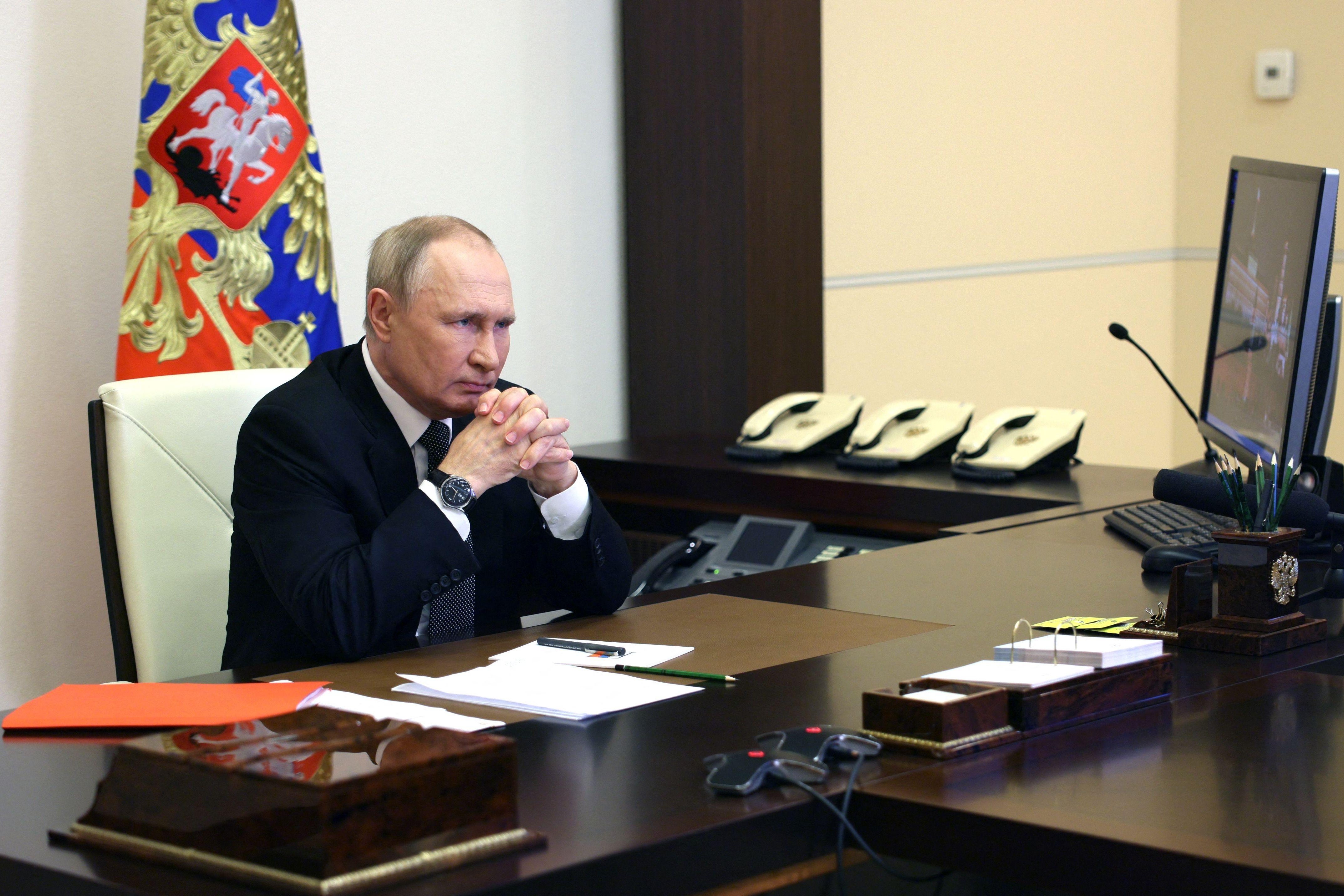 Vladimir Putin sits at a large desk, his elbows on the table, in front of a computer.