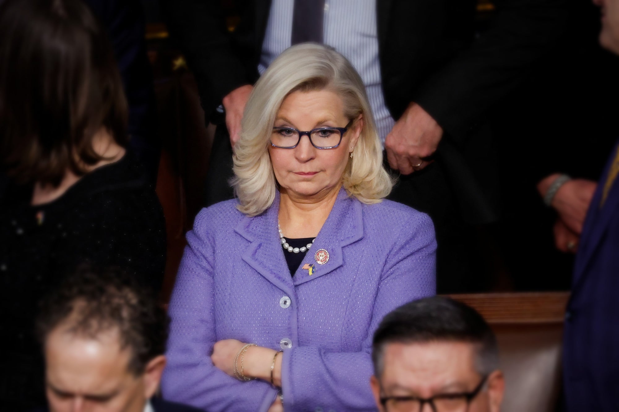 Liz Cheney, wearing lavender, looking on disapprovingly in a crowd of suited men.