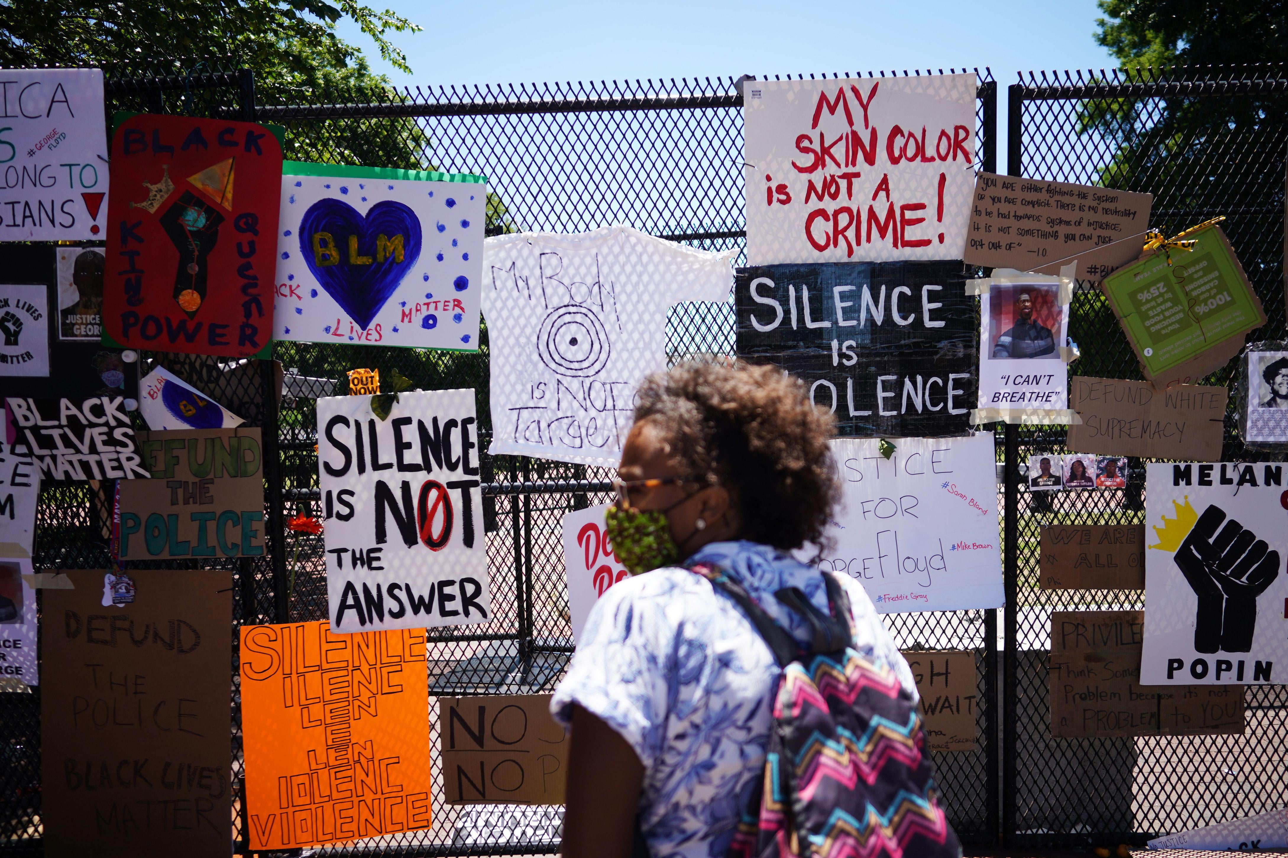 A woman stands in front of signs on the White House fence saying things like "Silence is not the answer."