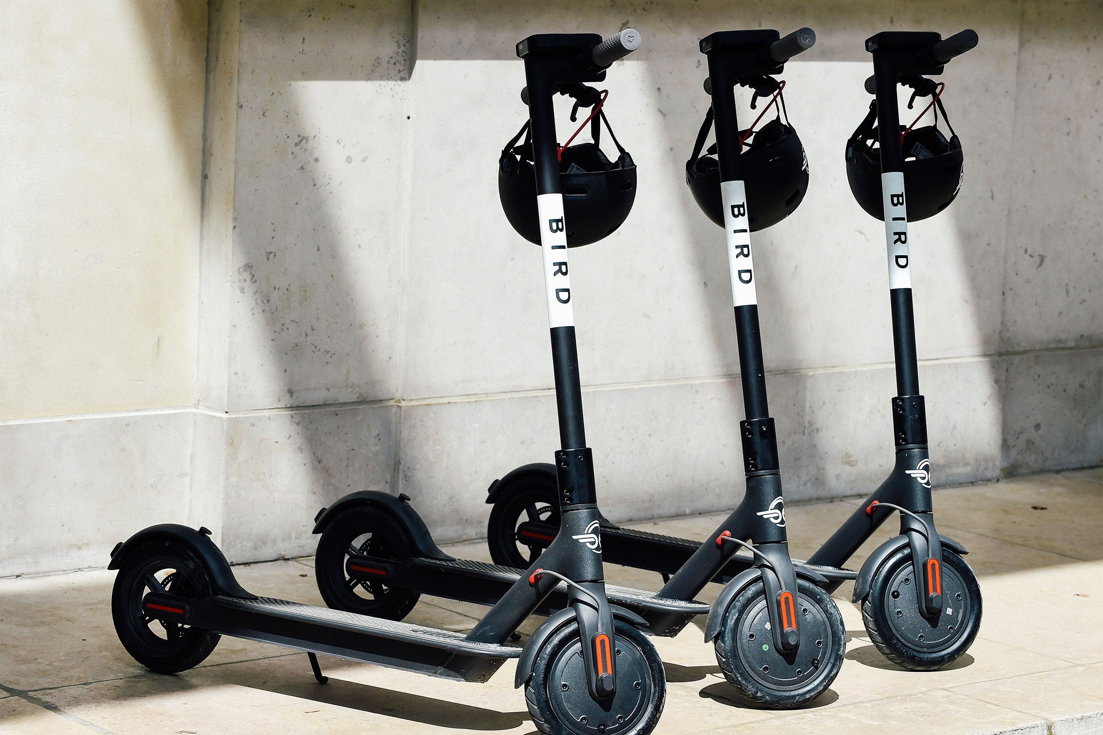 Three bird scooters with helmets hanging from the handlebars.