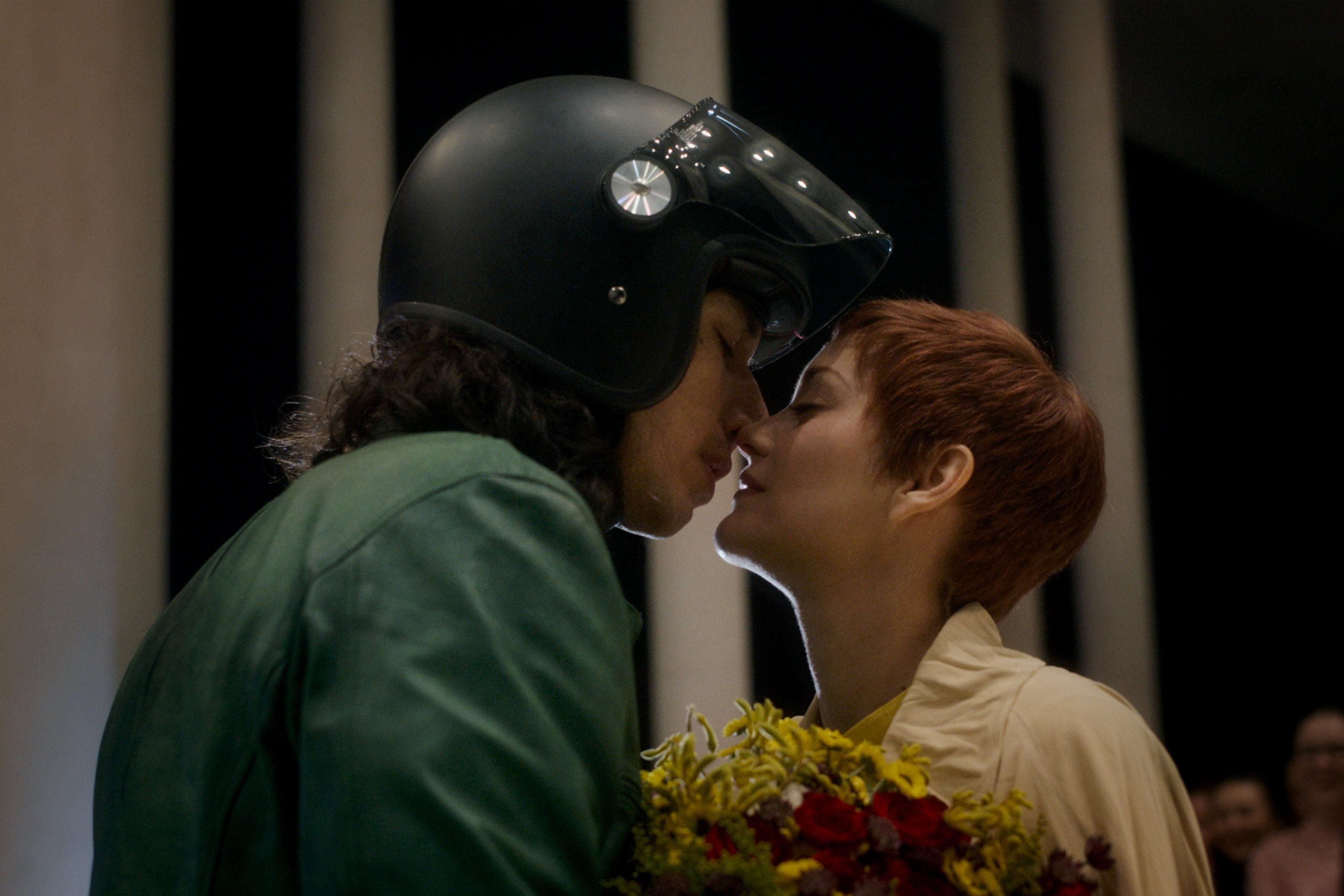 Adam Driver, wearing a motorcycle helmet, leans in to kiss Marion Cotillard in a still from Leos Carax's film Annette.