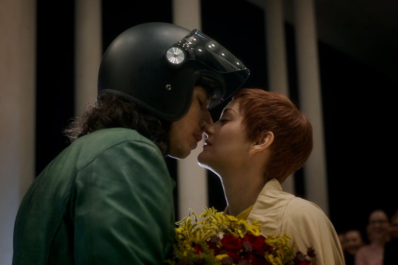 Adam Driver, wearing a motorcycle helmet, leans in to kiss Marion Cotillard in a still from Leos Carax's film Annette.