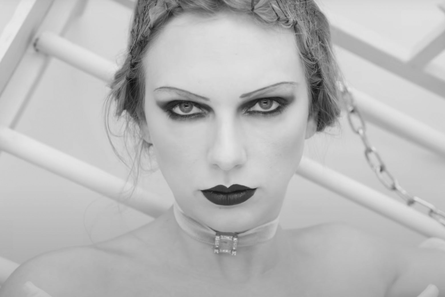 Taylor Swift looks directly at the camera and is wearing lots of black eyeshadow and black lipstick in a black-and-white photo. 