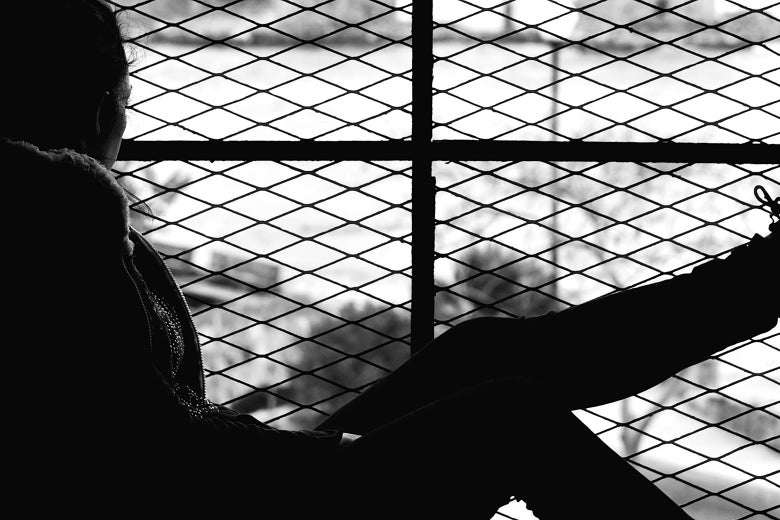 A silhouette of a woman sitting in front of a barred window.