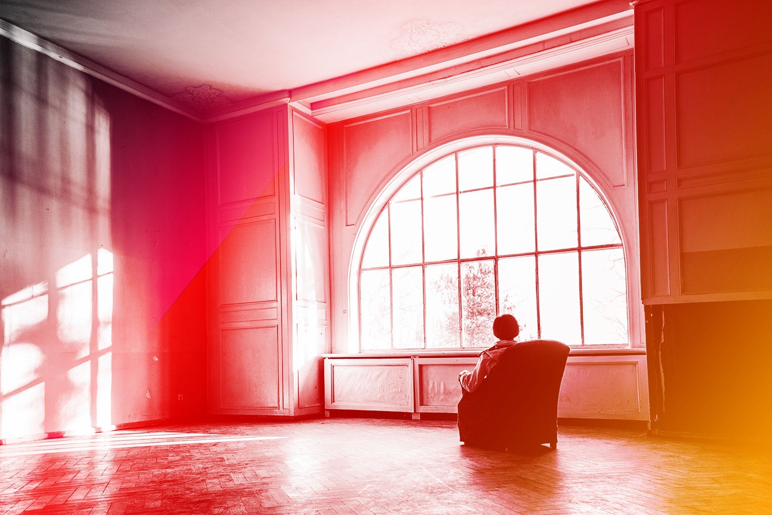 A woman sits alone in a massive room with sunlit windows.