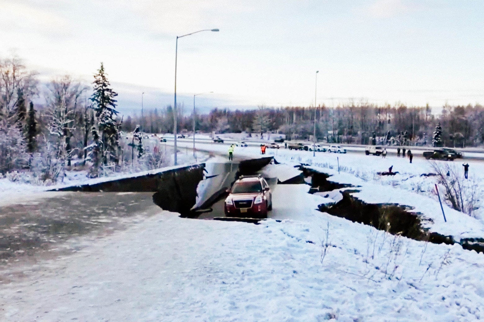 A crevasse splits a road off a snowy highway, with one car stuck in a depression