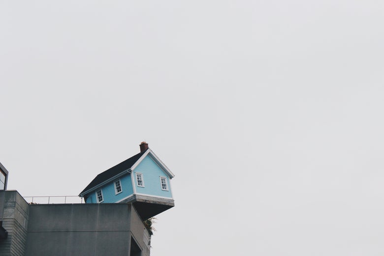 A robin's egg blue house perched on a ledge, where it is definitely not supposed to be.