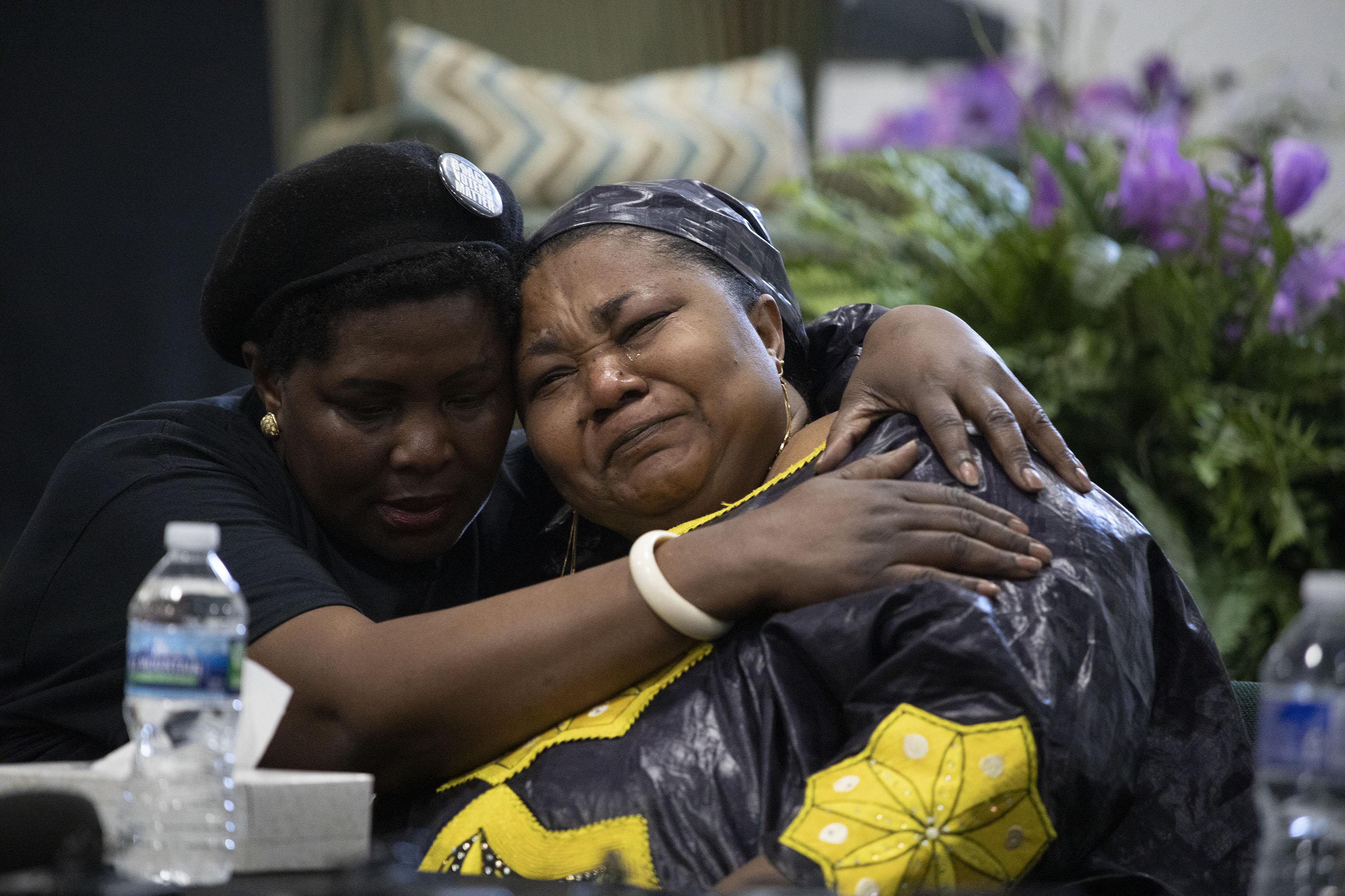 A woman leans and cries on the shoulder of another woman holding her, to her right.