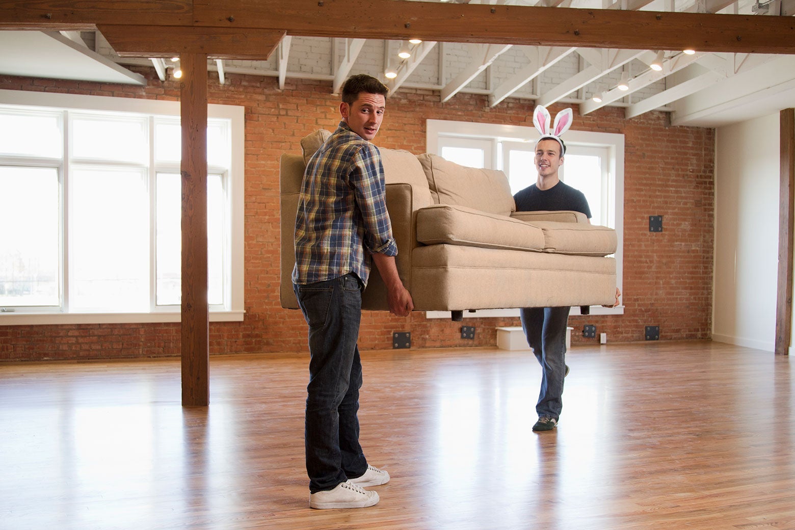 Two people moving a couch, but one has been illustrated to wear bunny ears.