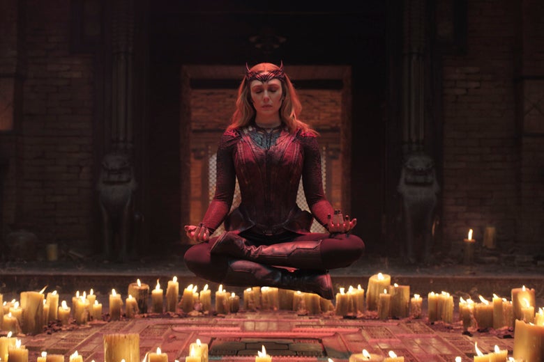 Elisabeth Olsen as Wanda, her legs criss cross apple sauce, hovers above a circle of candles, wearing a demonic red outfit and crown.