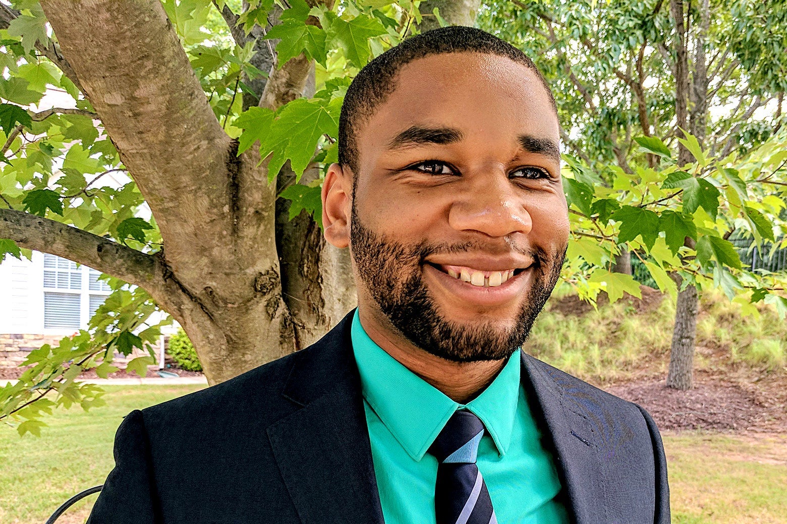 LeeQuan McLaurin smiles in a suit and tie in front of a tree.