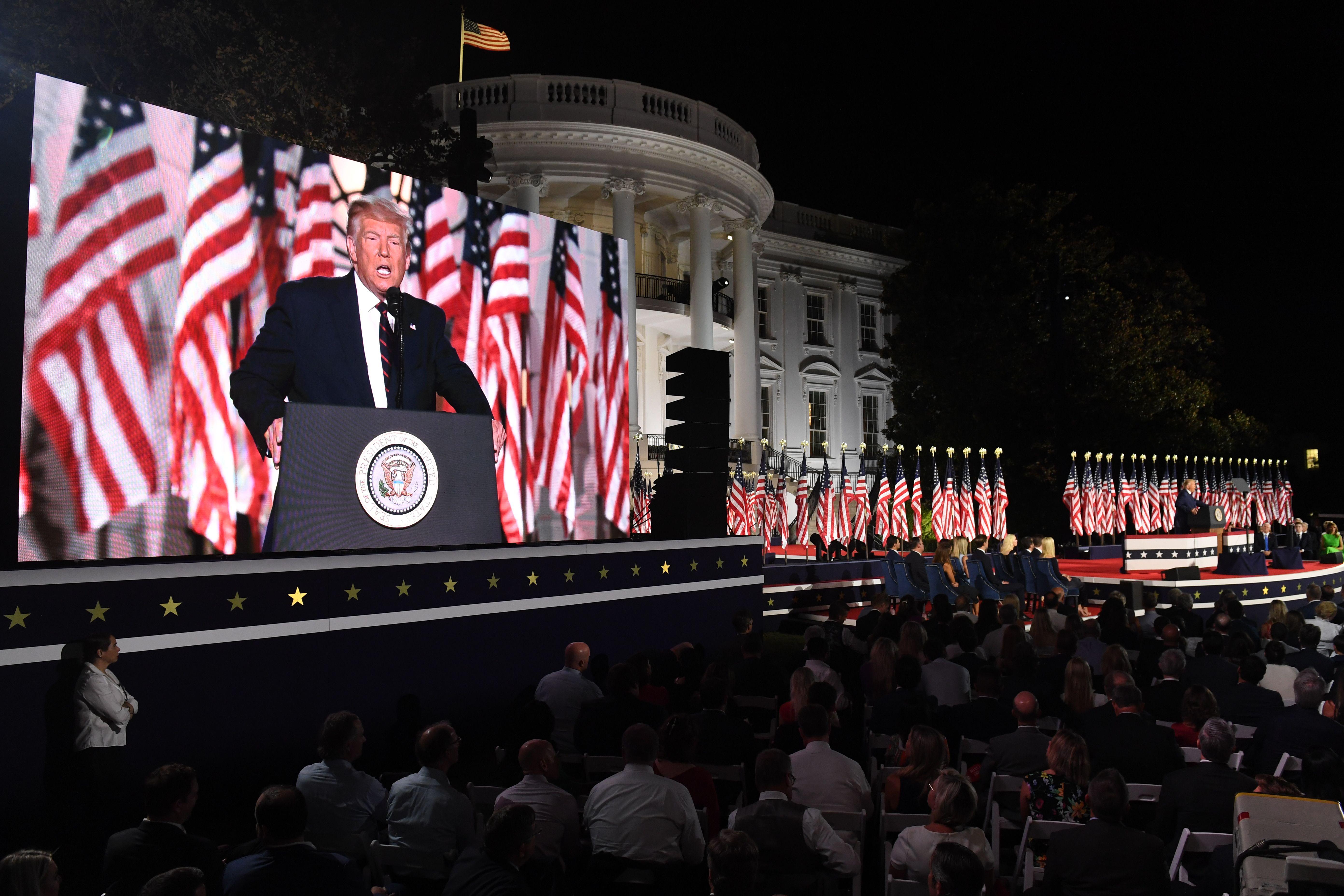 Trump appears on a jumbo screen on the White House lawn, with the White House behind him.