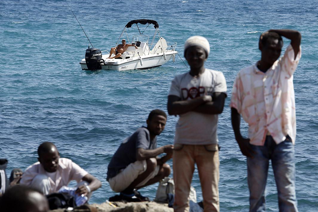 A man fishes from his boat as a group of migrants gather on the sea wall at the Saint Ludovic border crossing on the Mediterranean Sea between Ventimiglia, Italy, and Menton, France, on June 14, 2015