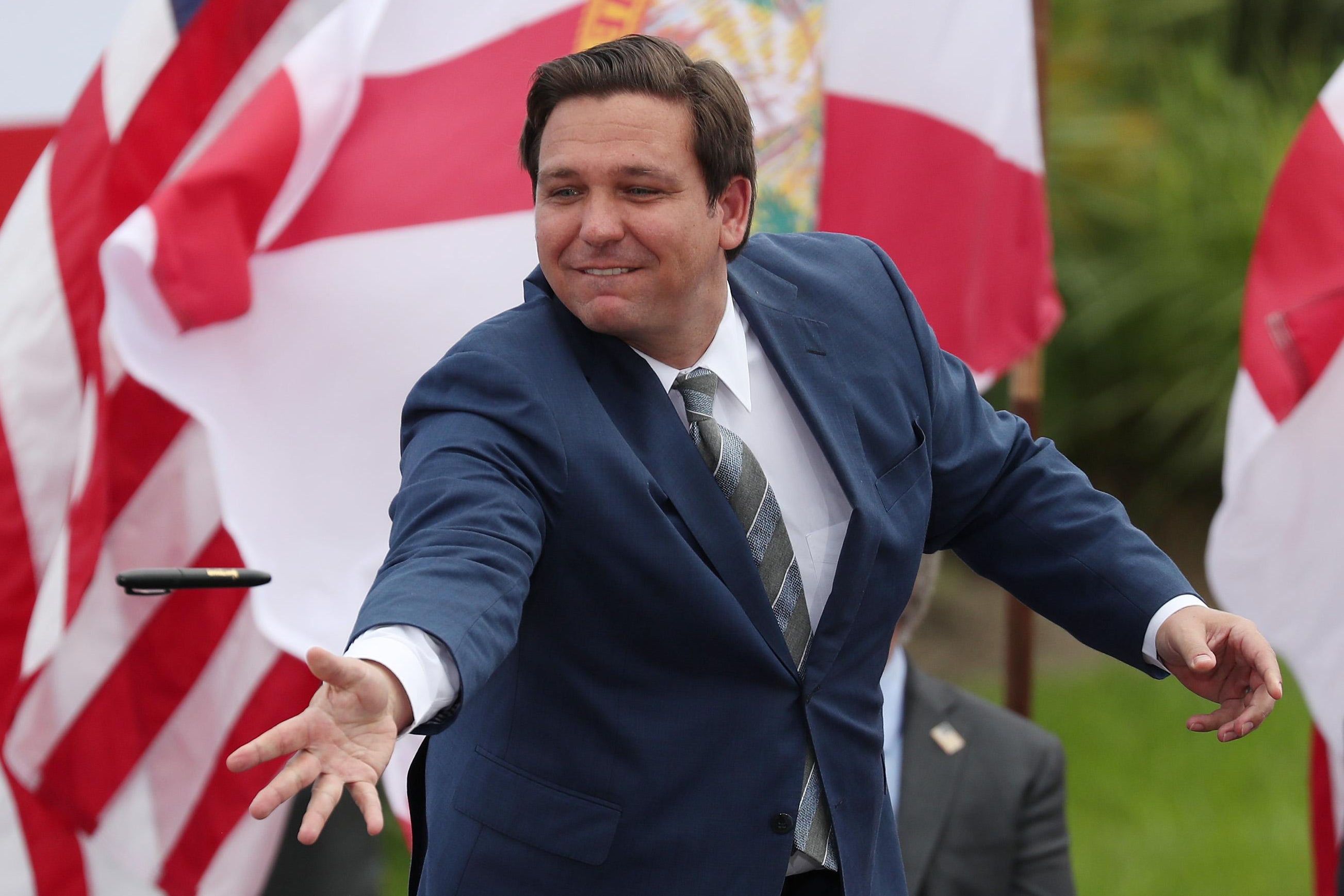 Ron DeSantis throws a black pen, with an American flag and a Florida state flag behind him.