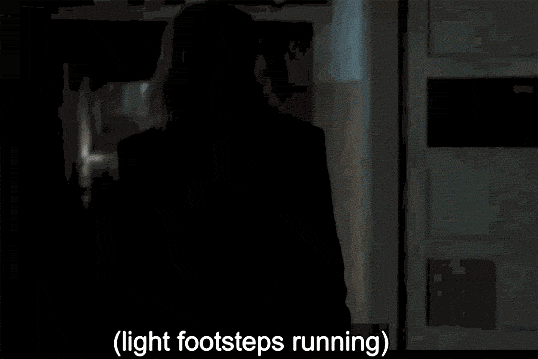 Lydia, wearing all black, walks down a hallway and turns around, scared.