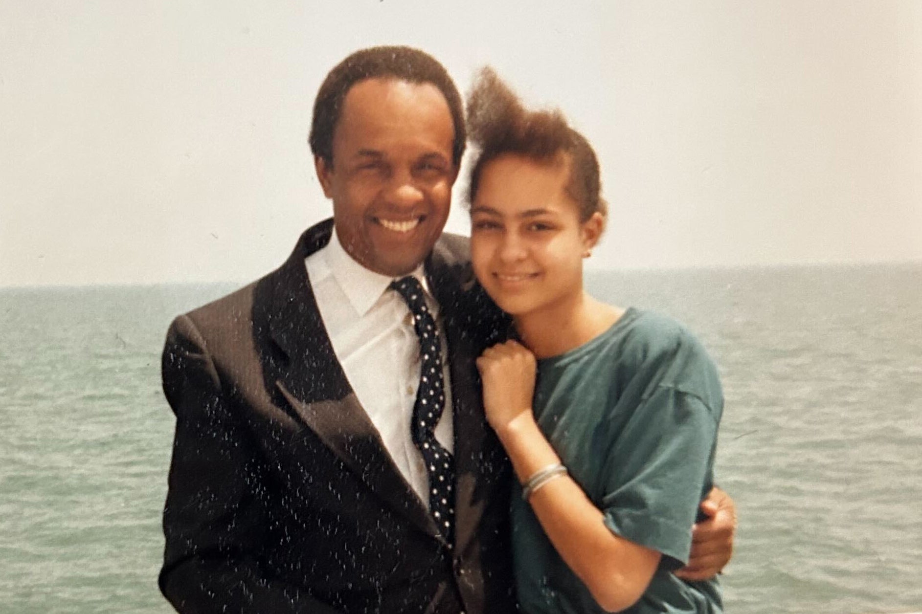 A father and daughter smiling and posing by the water.