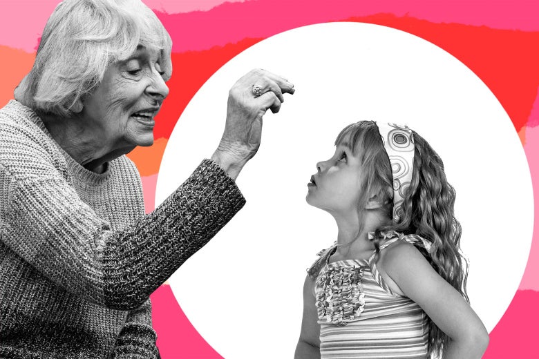 An older woman holds something in her fingers over a curious-looking little girl.
