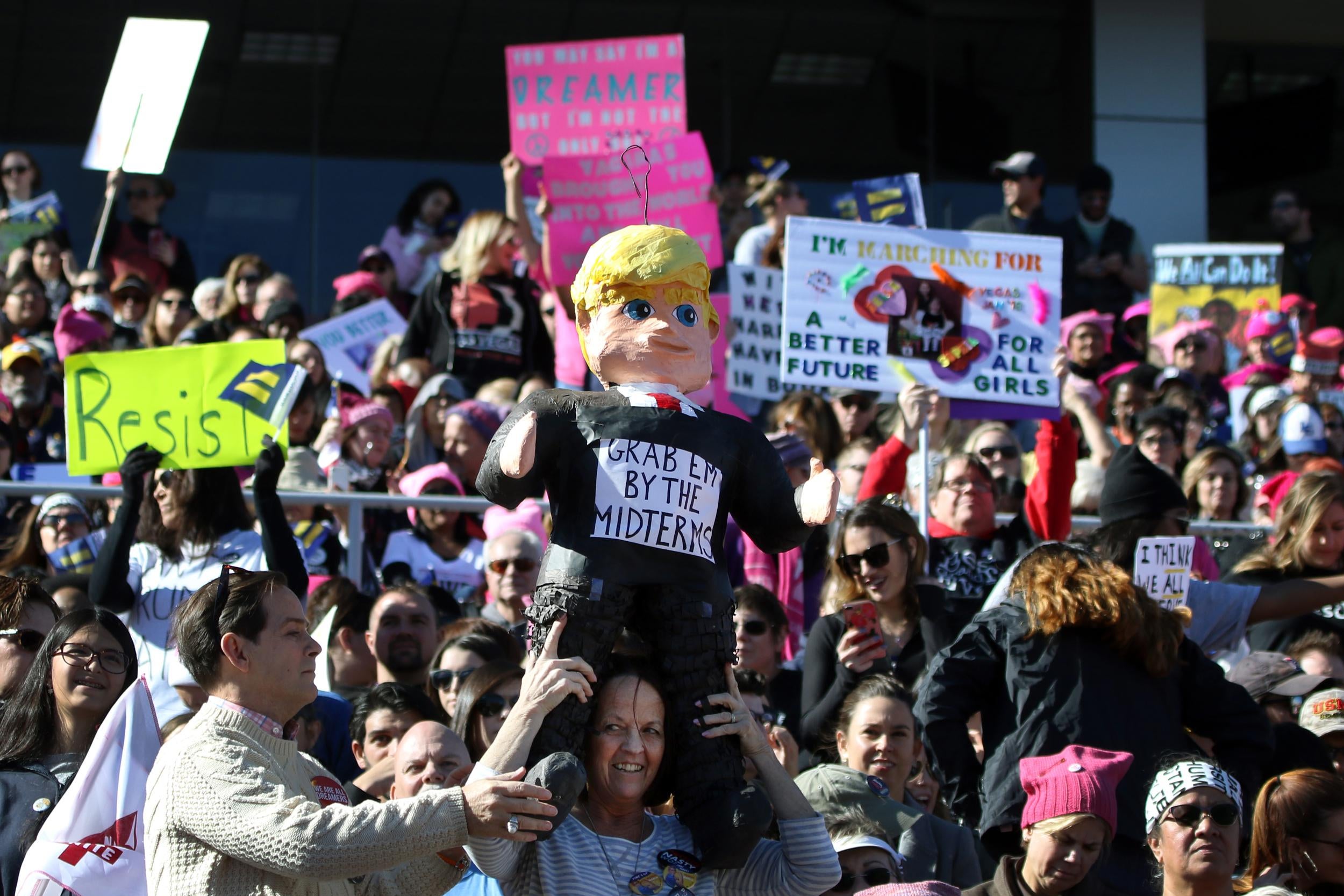 Participants, one with a US President Donald Trump figure, stand strong and applaud with their signs during the Women's March Anniversary 'Power To The Polls' event, January 21, 2018 at Sam Boyd Stadium in Las Vegas, Nevada.The rally is aimed at starting a national campaign to register voters, increase support for women and secure progressive seats in the upcoming midterm elections.