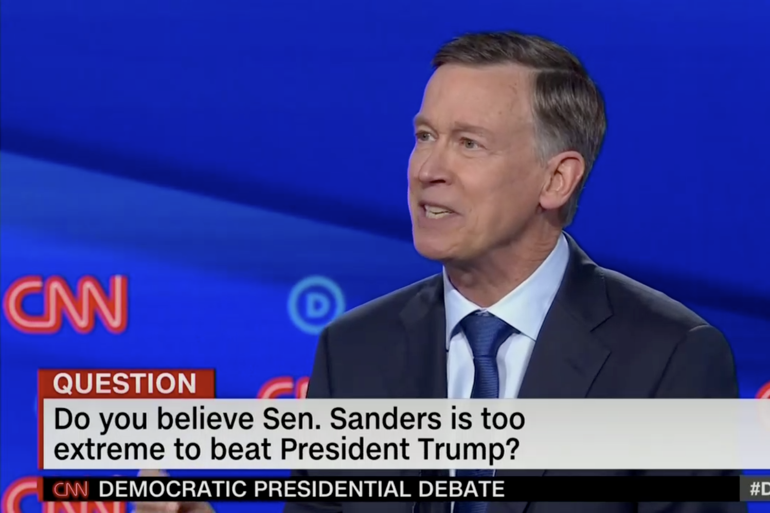 In this screengrab from CNN, John Hickenlooper debates. The banner reads: "Do you believe Sen. Sanders is too extreme to beat President Trump?"