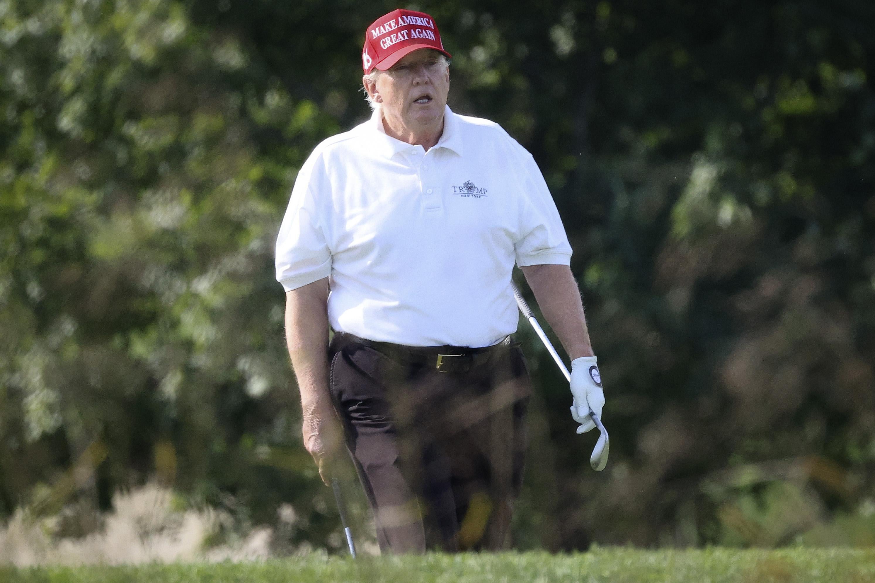 Donald Trump holding a golf club and wearing a MAGA hat, looking pretty terrible.