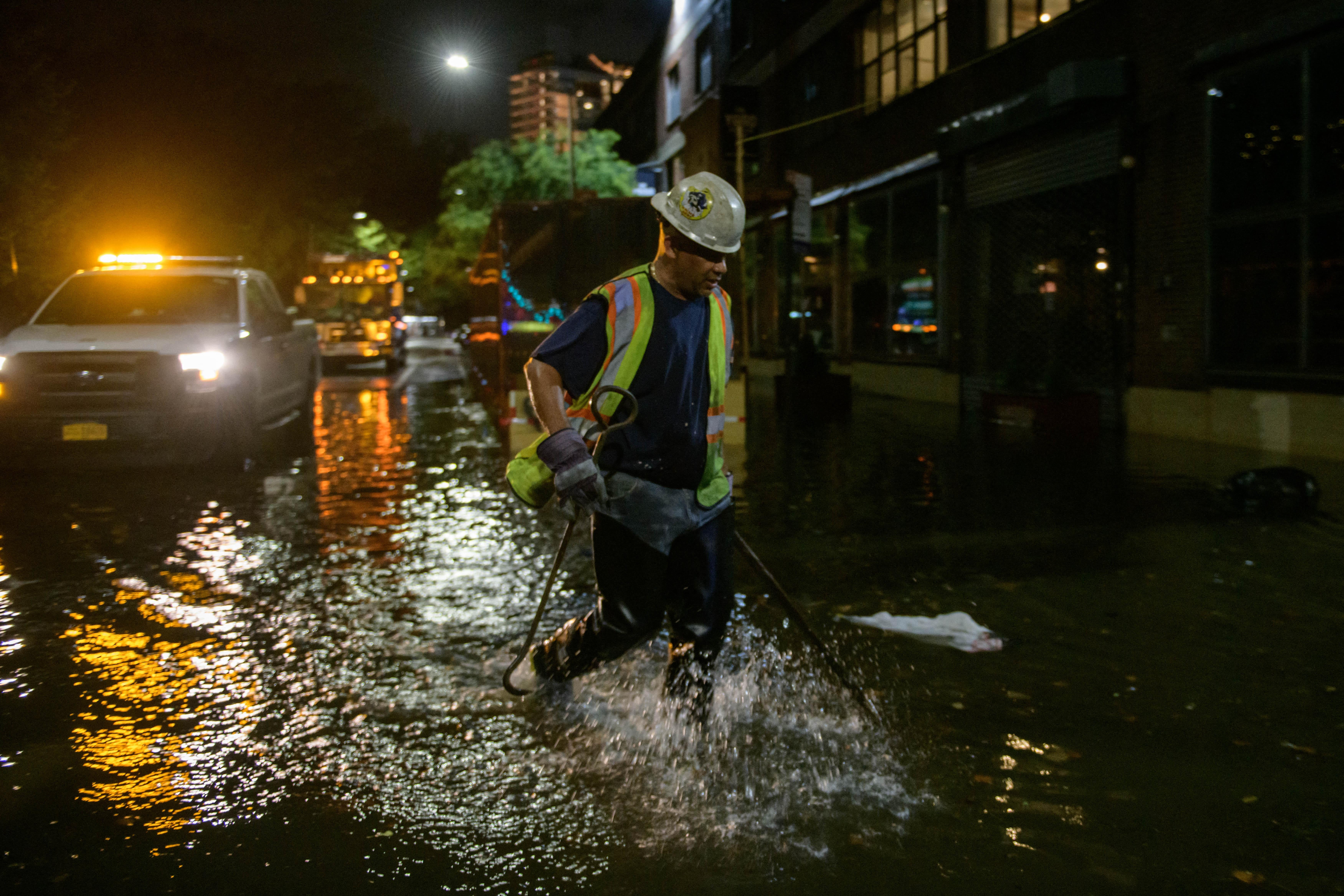 A worker unblocks drains on a street affected by floodwater in Brooklyn, New York early on September 2, 2021, as flash flooding and record-breaking rainfall brought by the remnants of Storm Ida swept through the area. 