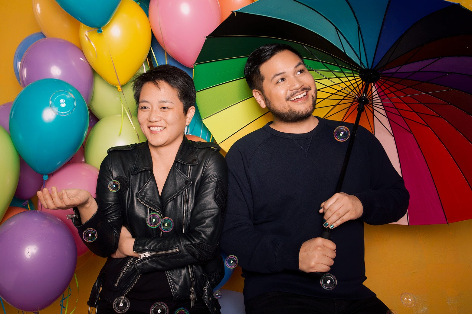 Kathy Tu and Tobin Low, with balloons of many colors in the background. Low holds a rainbow umbrella.