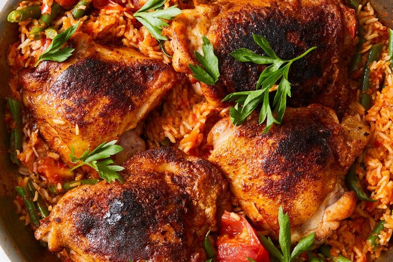 Paprika chicken thighs with rice, herbs, and green peppers in a skillet