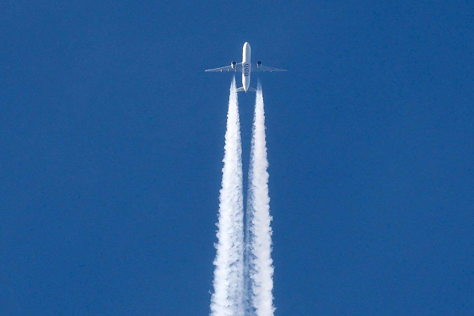 An aircraft in a blue sky, with a long line of contrails behind it. 