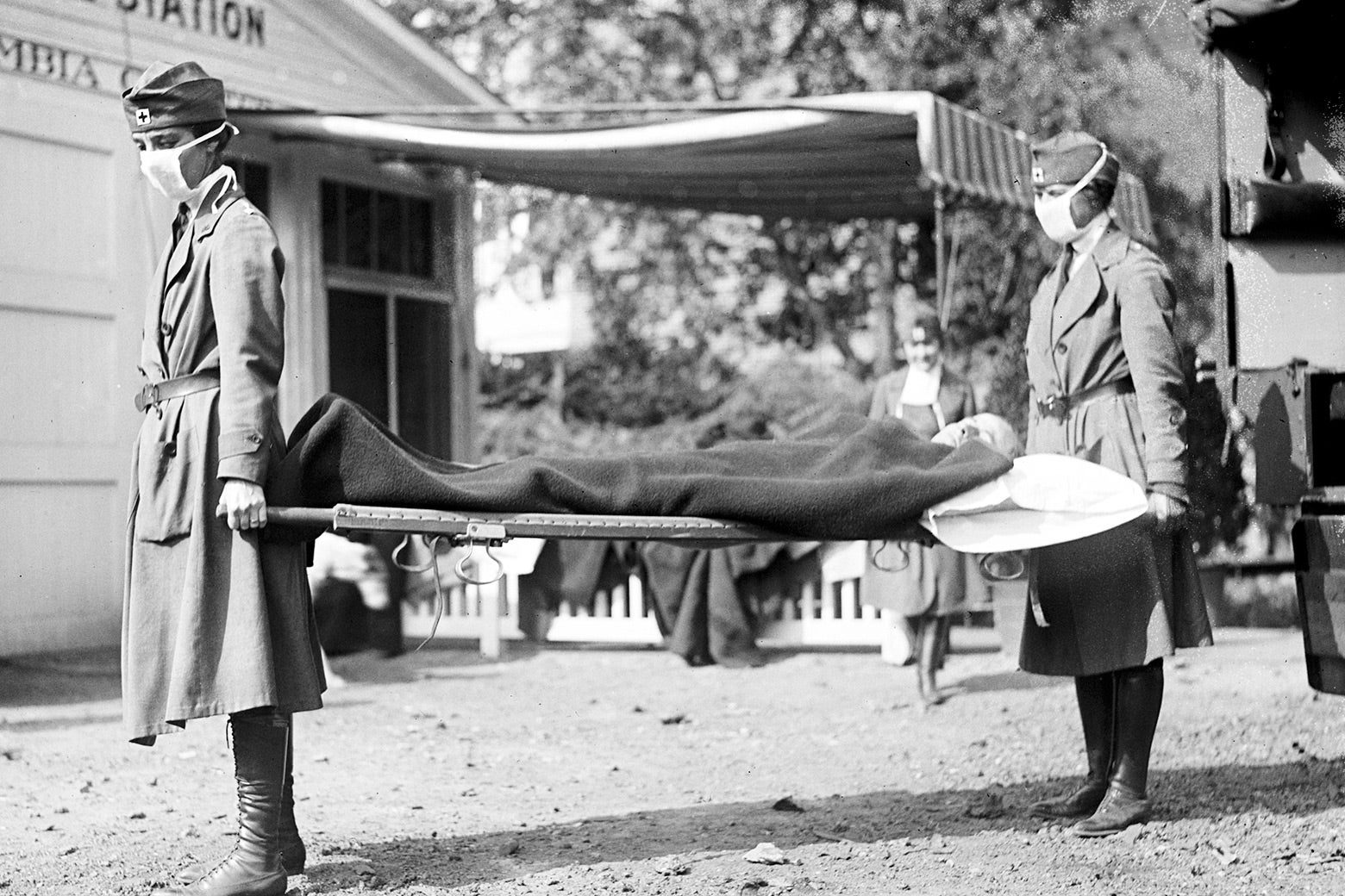 Two Red Cross workers carry a stretcher in a black-and-white photo.