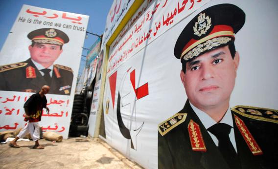 Salah Abdel Moneim, 40, an Anti-Mursi supporter of Egypt's army, walks in front of his shop, plastered with huge posters of Egypt's army chief General Abdel Fattah al-Sisi.