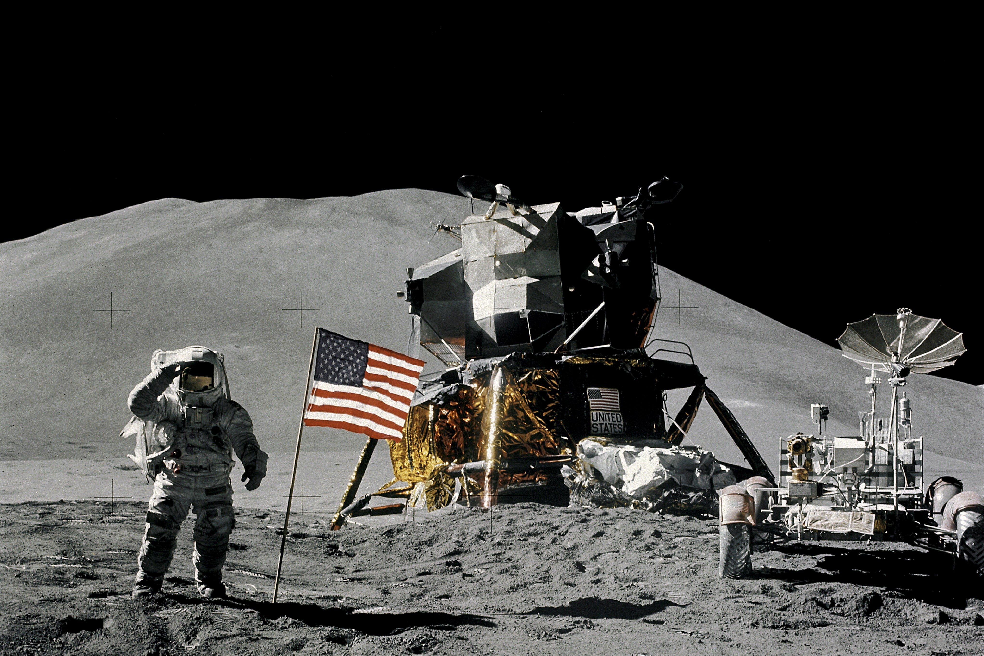 An astronaut on the moon salutes the camera while standing by an American flag and the lunar lander and rover.