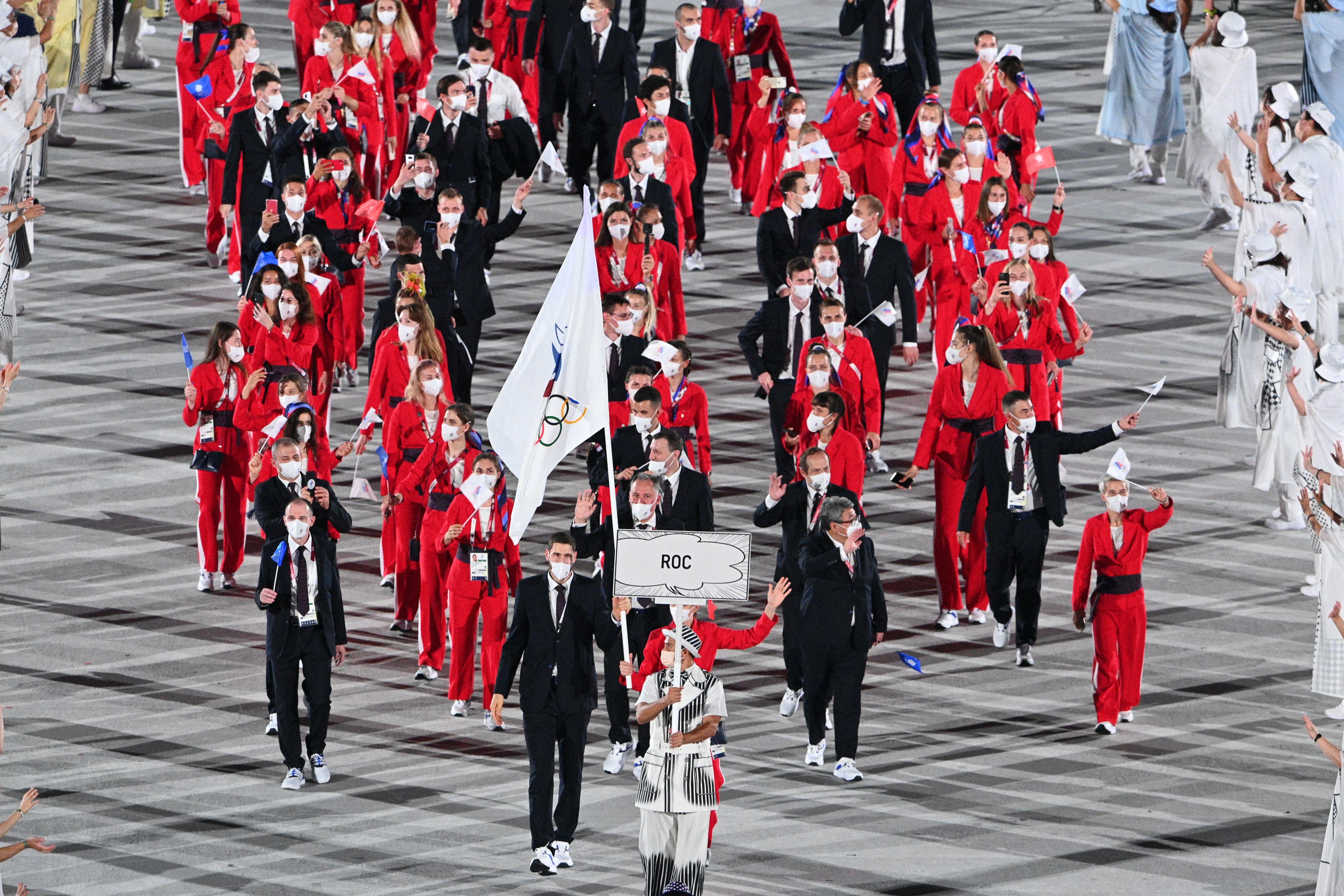 A large group of Russian athletes wearing red and black march in the Olympic stadium
