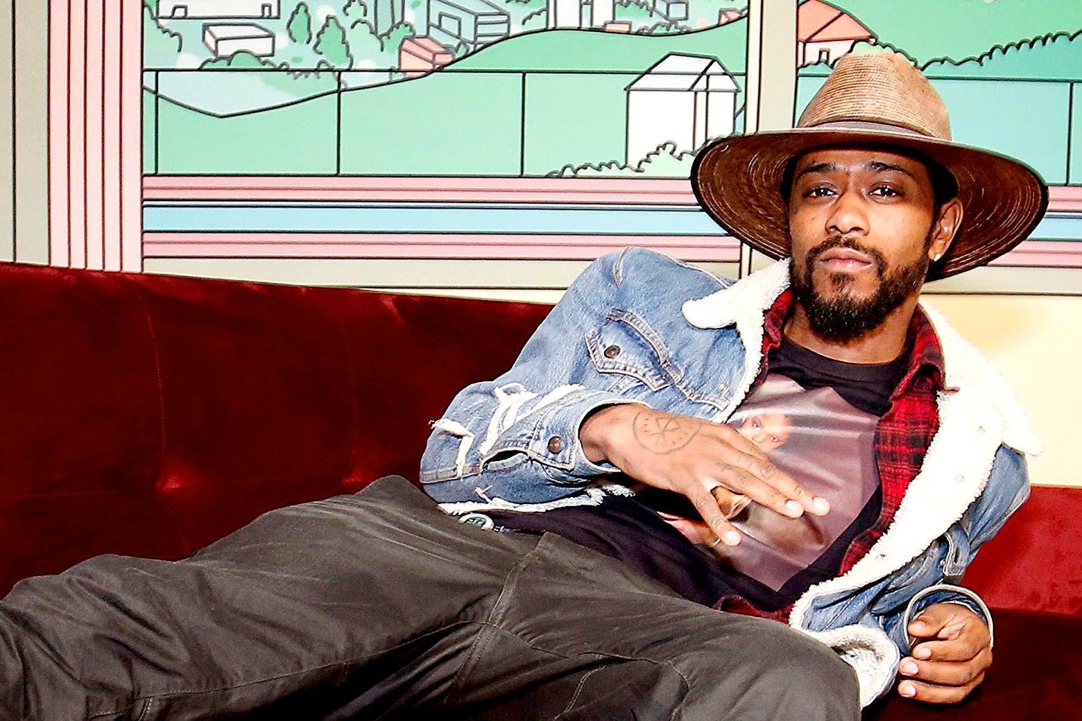 Lakeith Stanfield wearing a hat and relaxing on a couch.