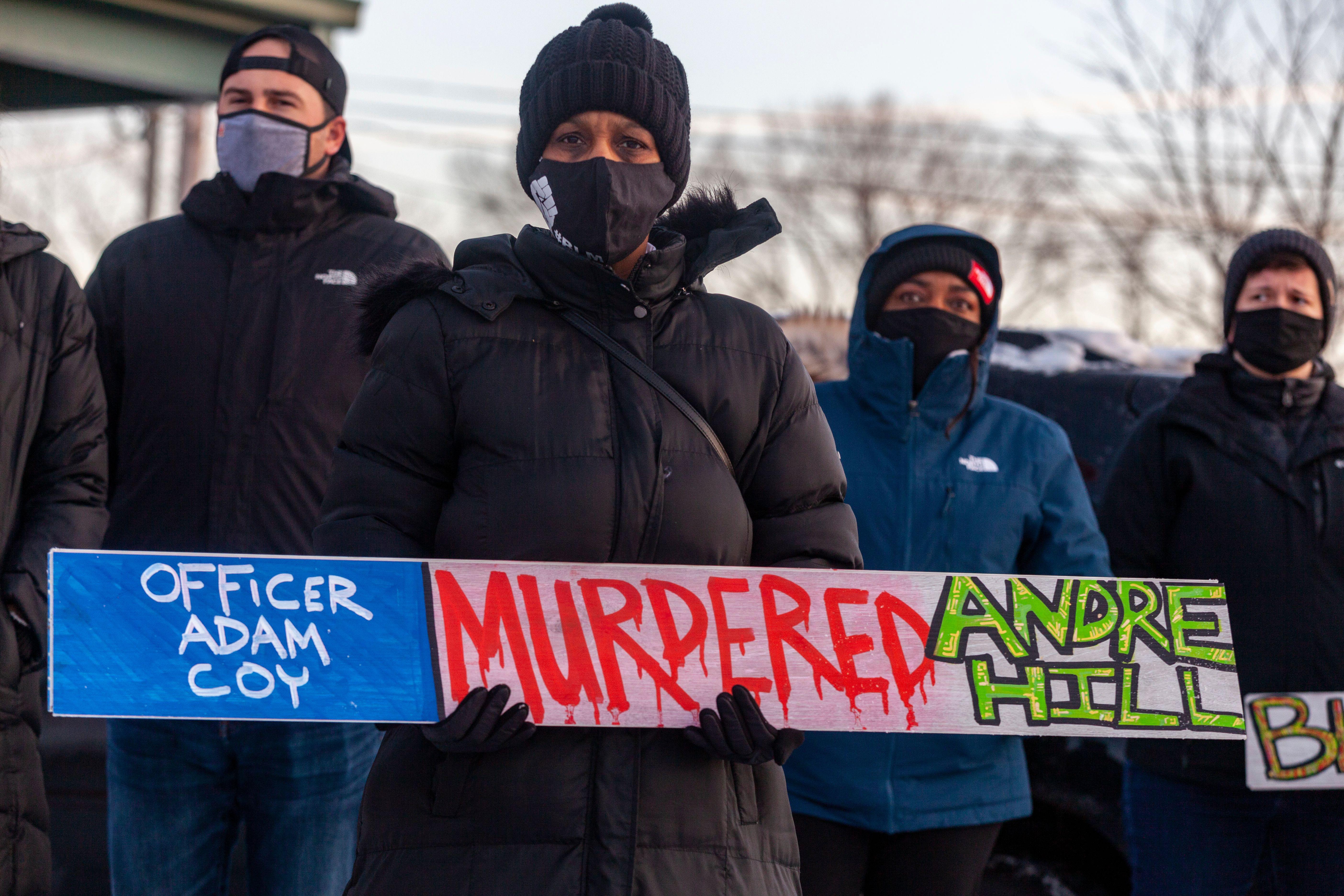A demonstrator standing in a crowd holds a sign condemning Officer Adam Coy