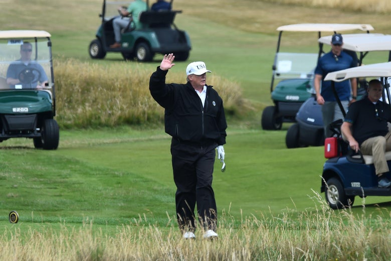 Trump, dressed in black exercise-type clothes, waves. Five golf carts can be seen around him. 