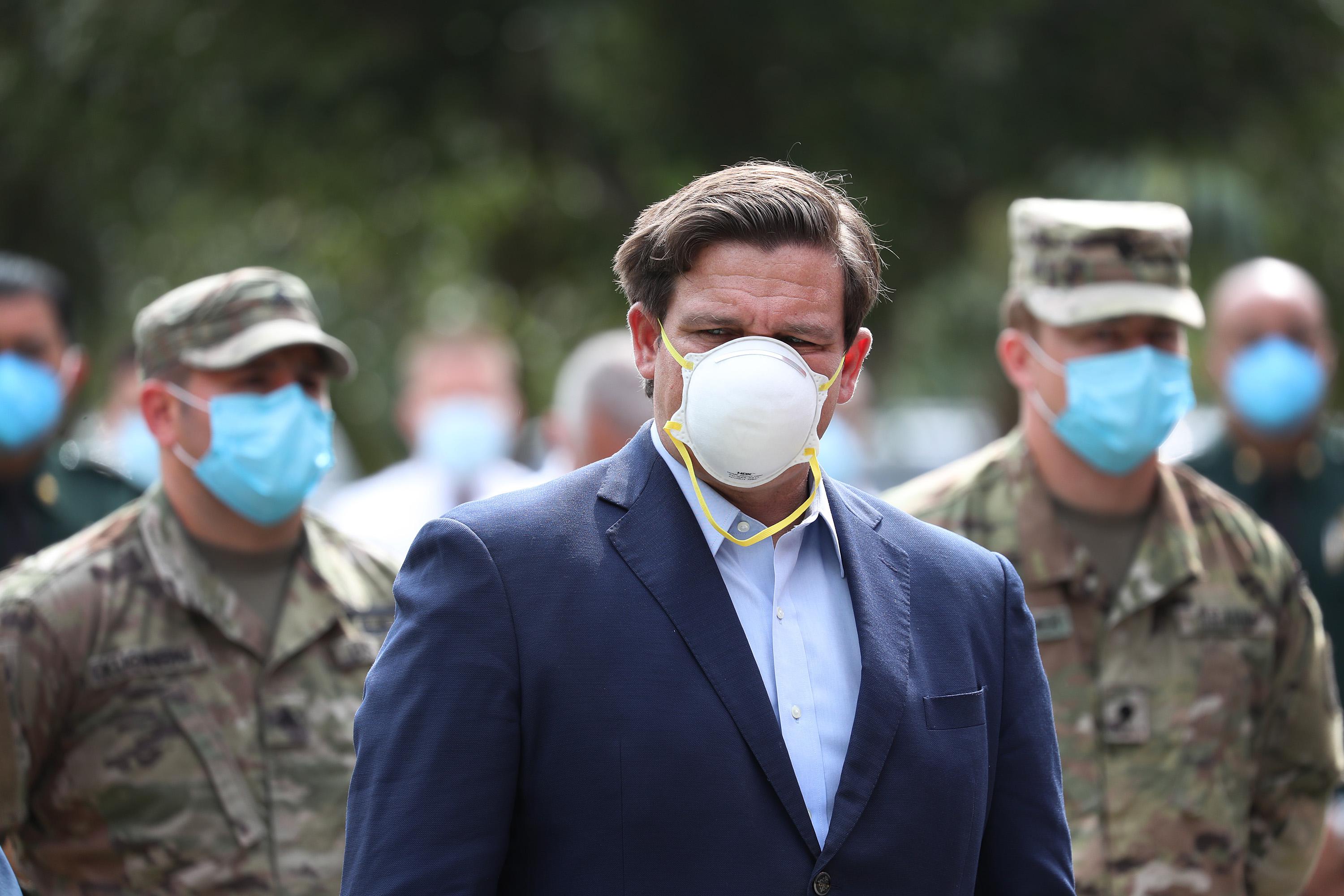 Ron DeSantis, wearing a mask, stands in front of National Guard members wearing masks