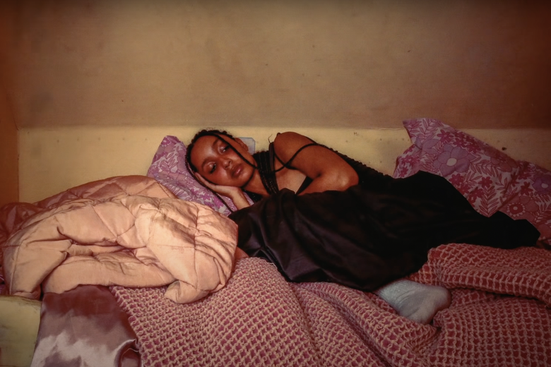 A woman lies curled up on her bed, her eyes closed and her head on her comforter.