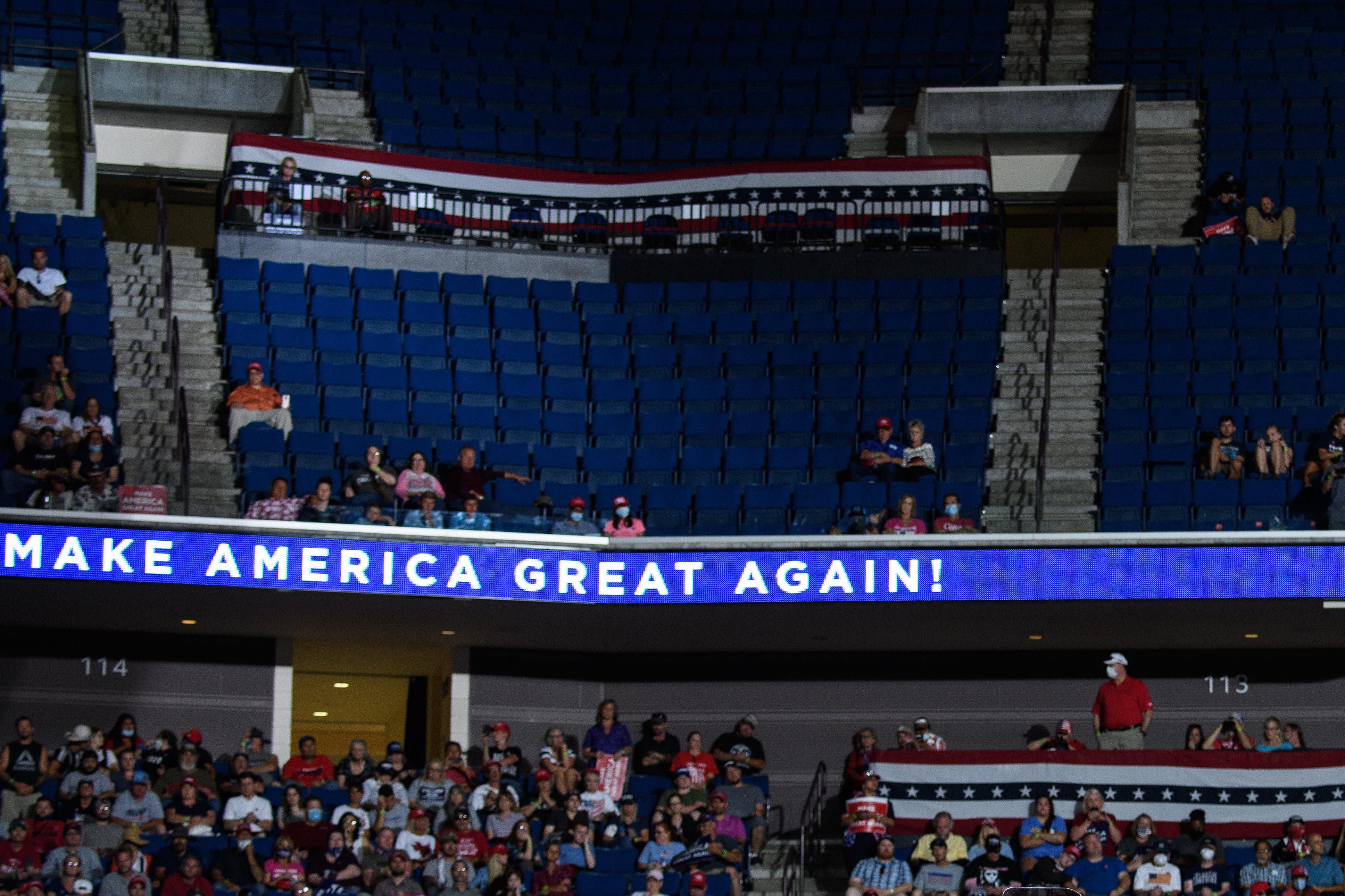 The largely empty upper section of an arena above an electronic sign that says "Make America Great Again."