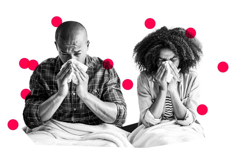 Man and woman sitting side by side both blowing their noses into tissues.