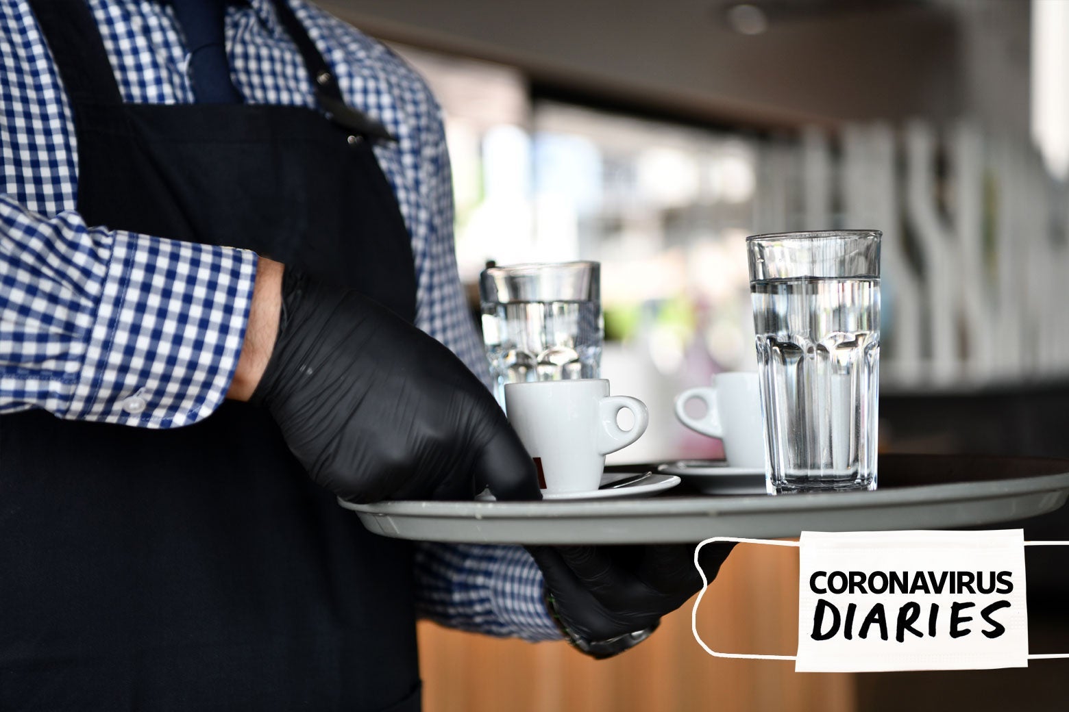 A waiter wearing gloves holds a tray of cups of water and espresso.