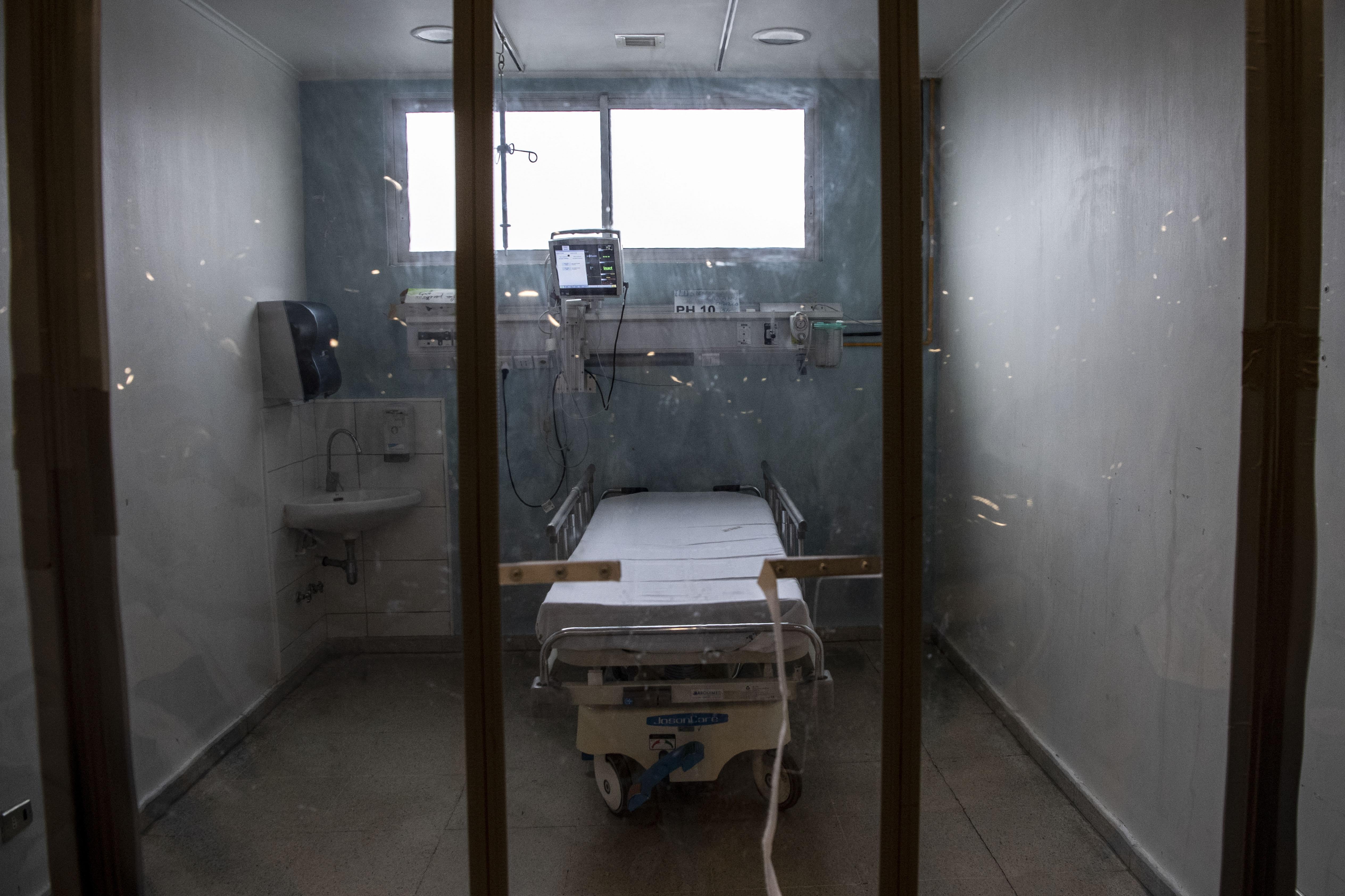An empty hospital bed is seen through glass frames.