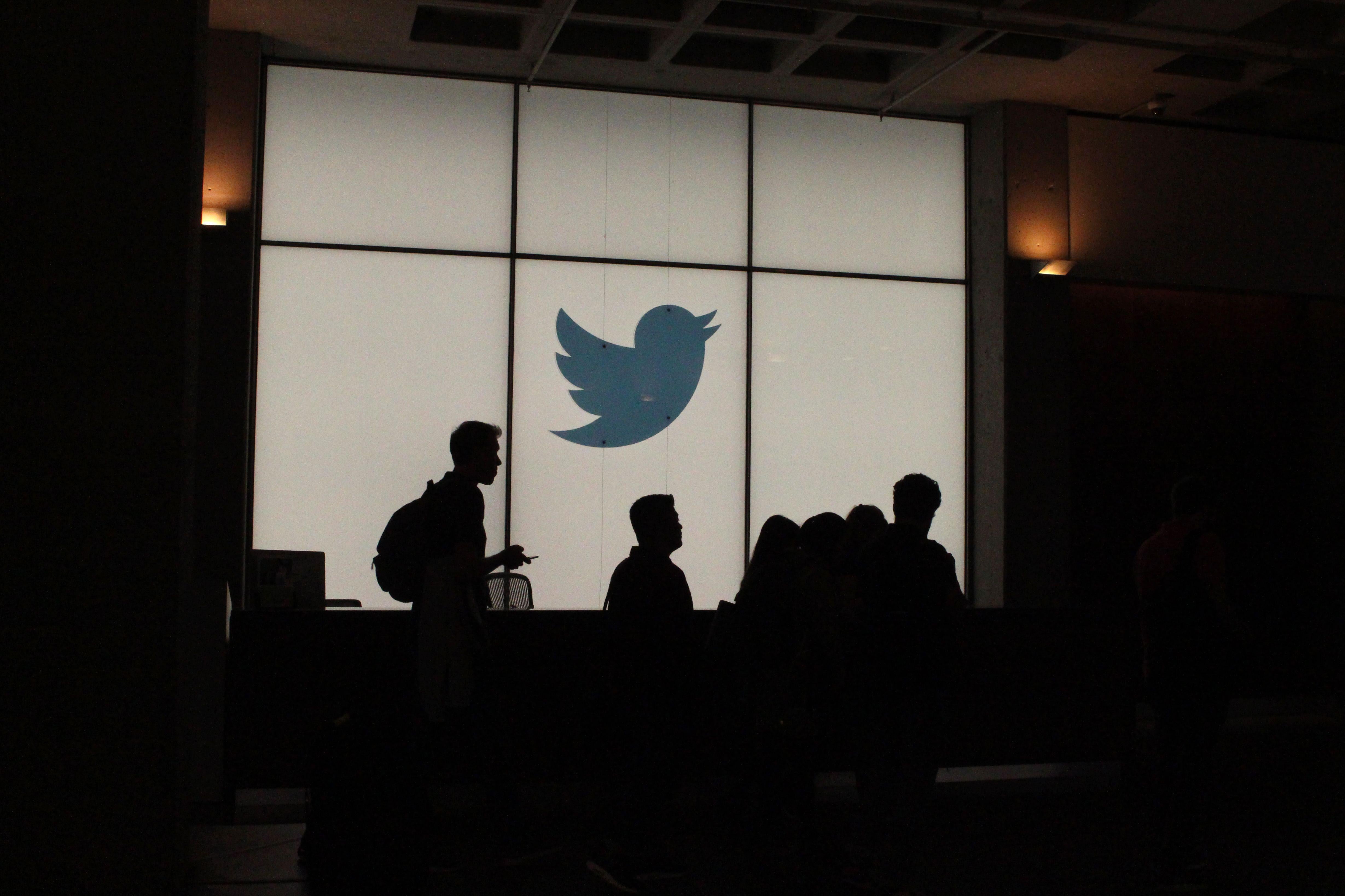 Silhouettes of employees walking by a lit up Twitter sign