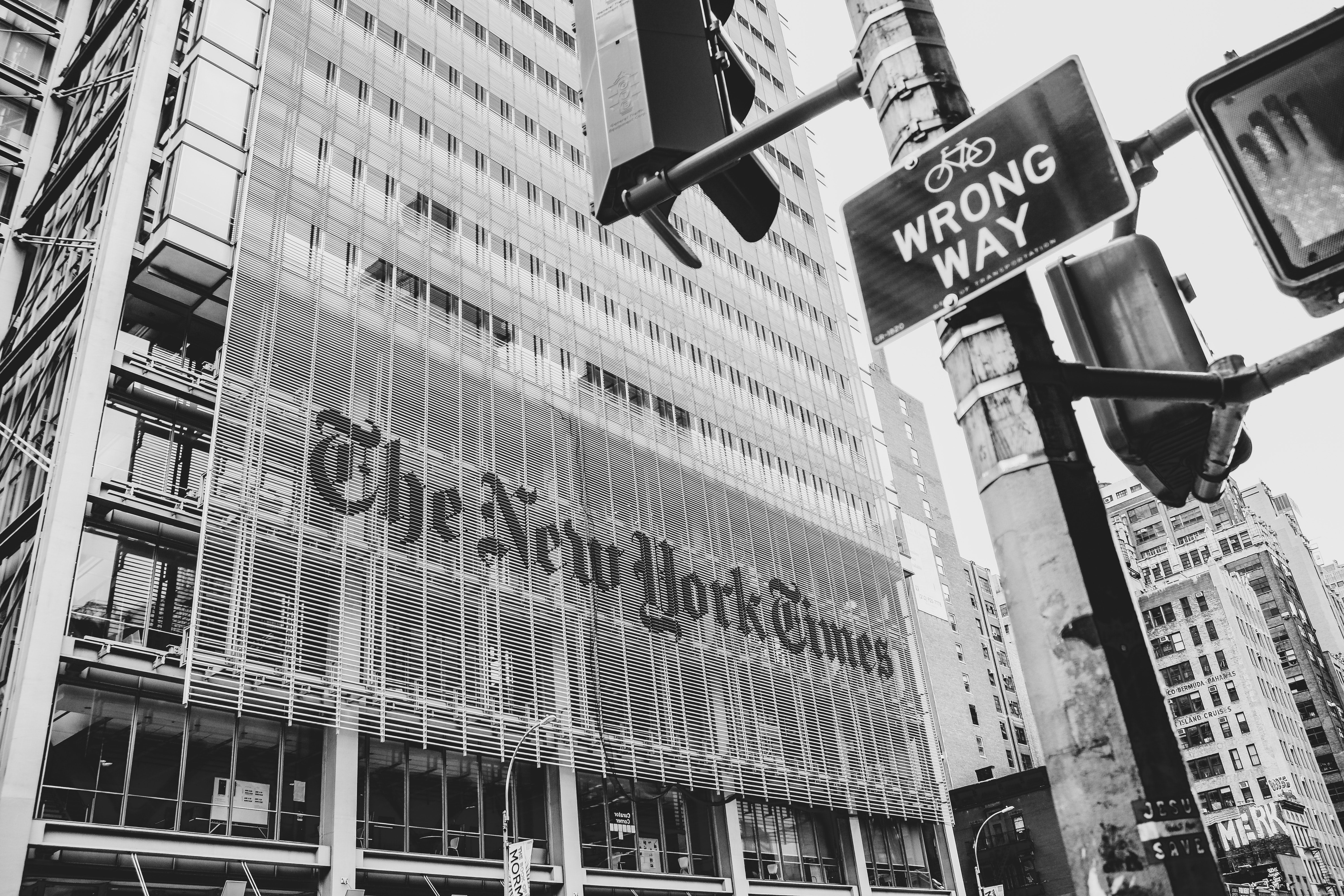 A black and white photo of a building that says The New York Times in lettering the size of a story or two. A sign on the street says "Wrong Way."