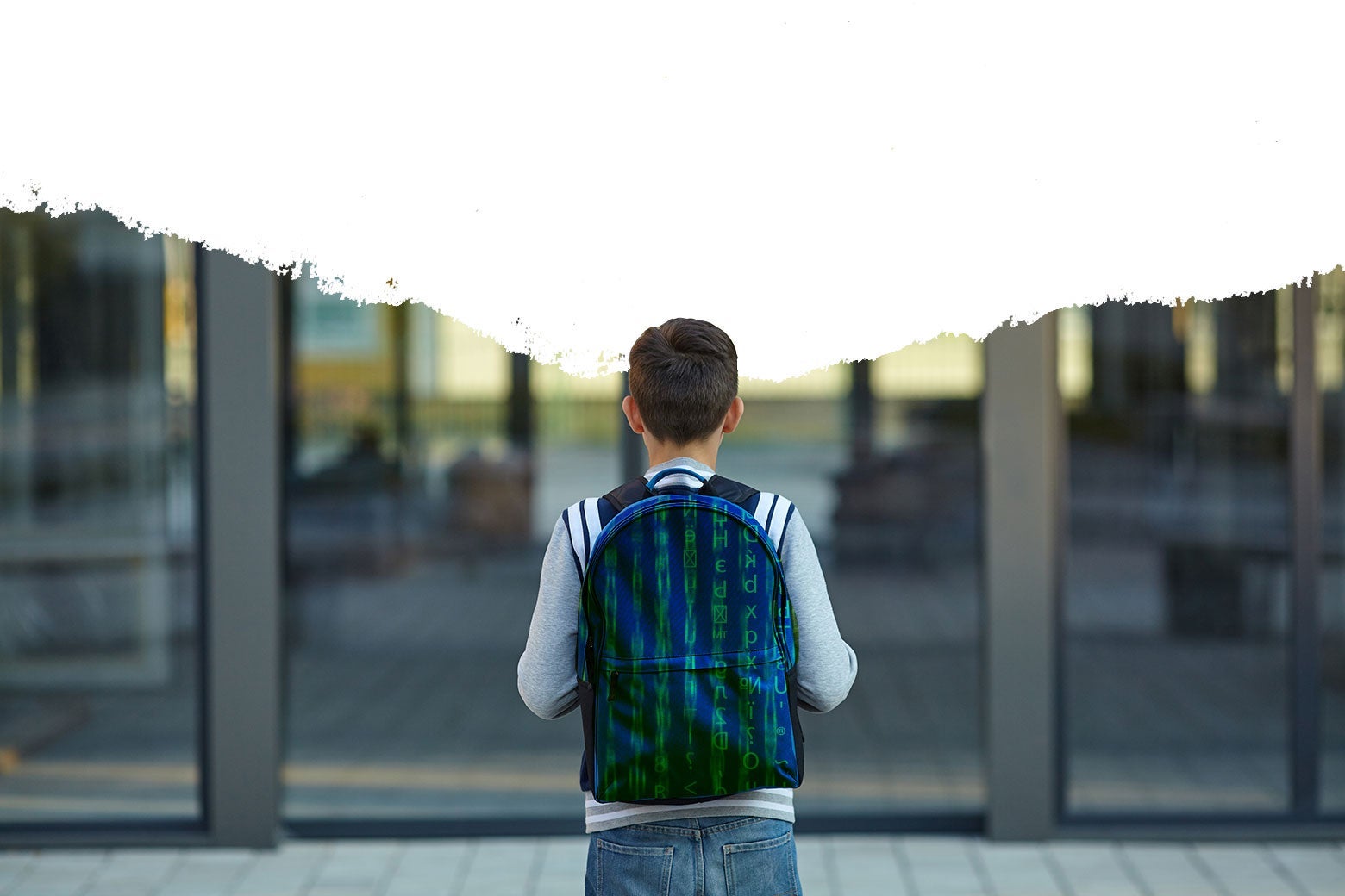 A kid walking into school wearing a backpack, with the top of the image erased.